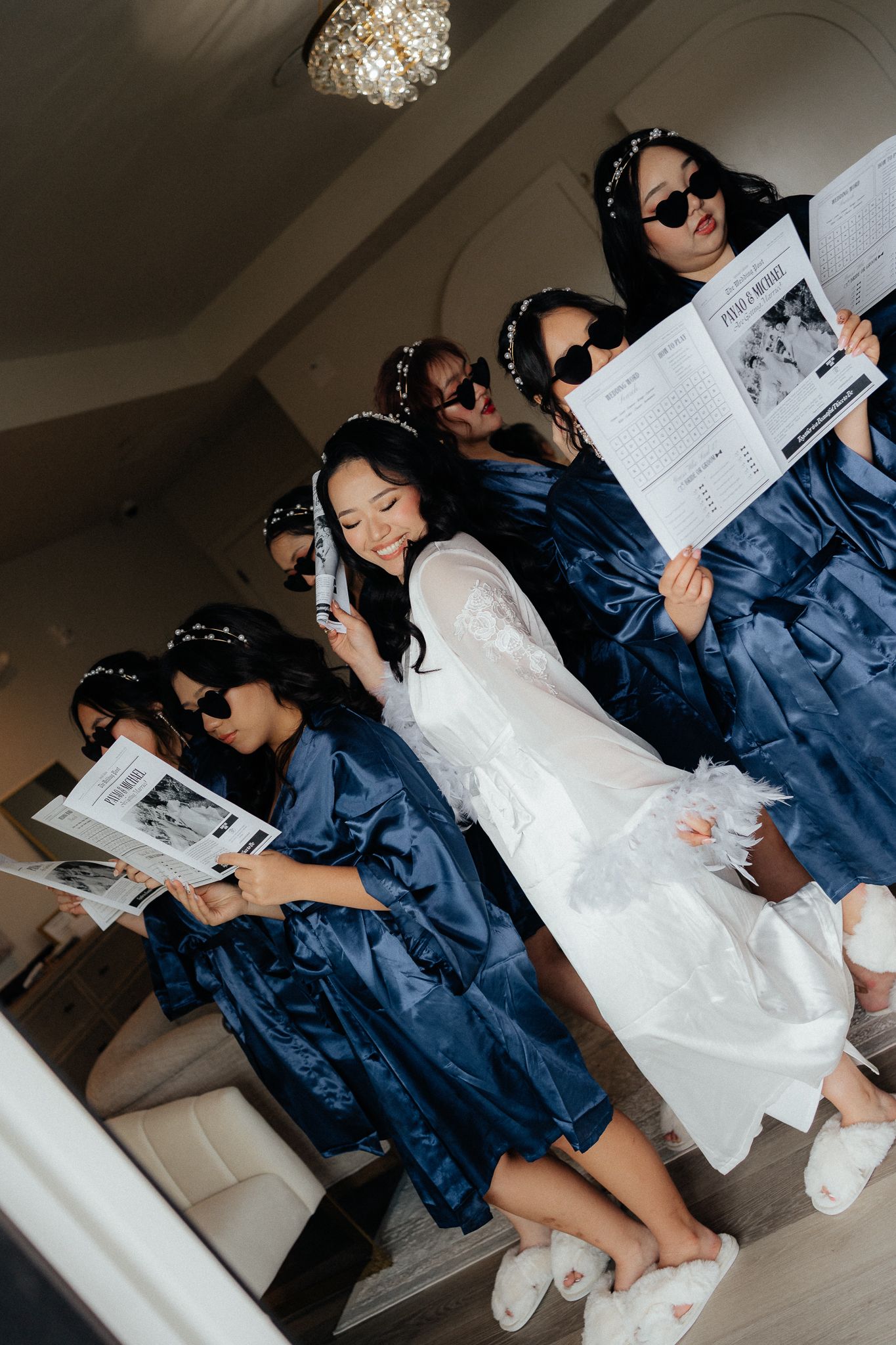Wedding party wearing navy blue robes and sunglasses posing with papers while bride wears white in center.
