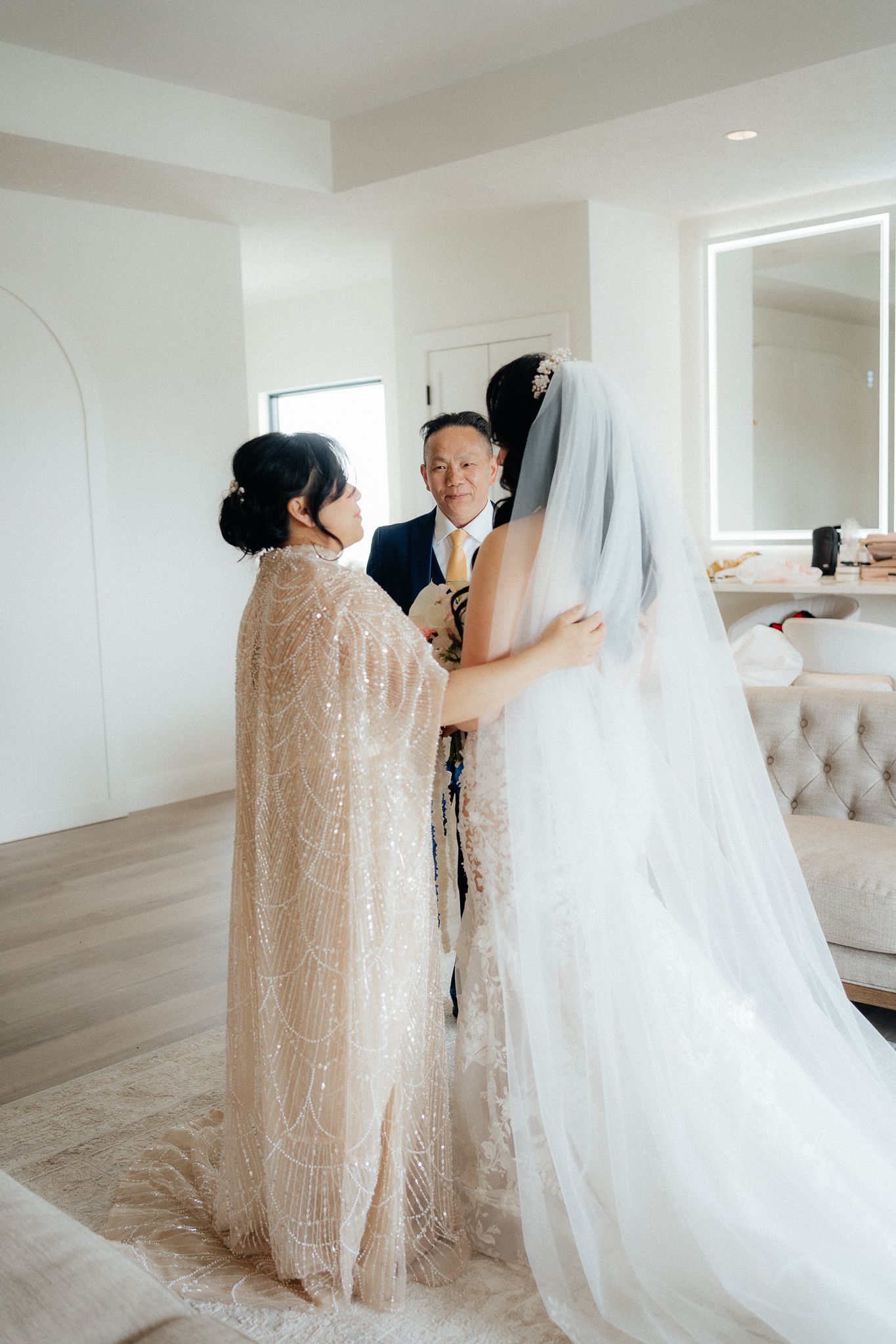 A wedding preparation scene showing a dress fitting with a long lace gown and flowing white veil.