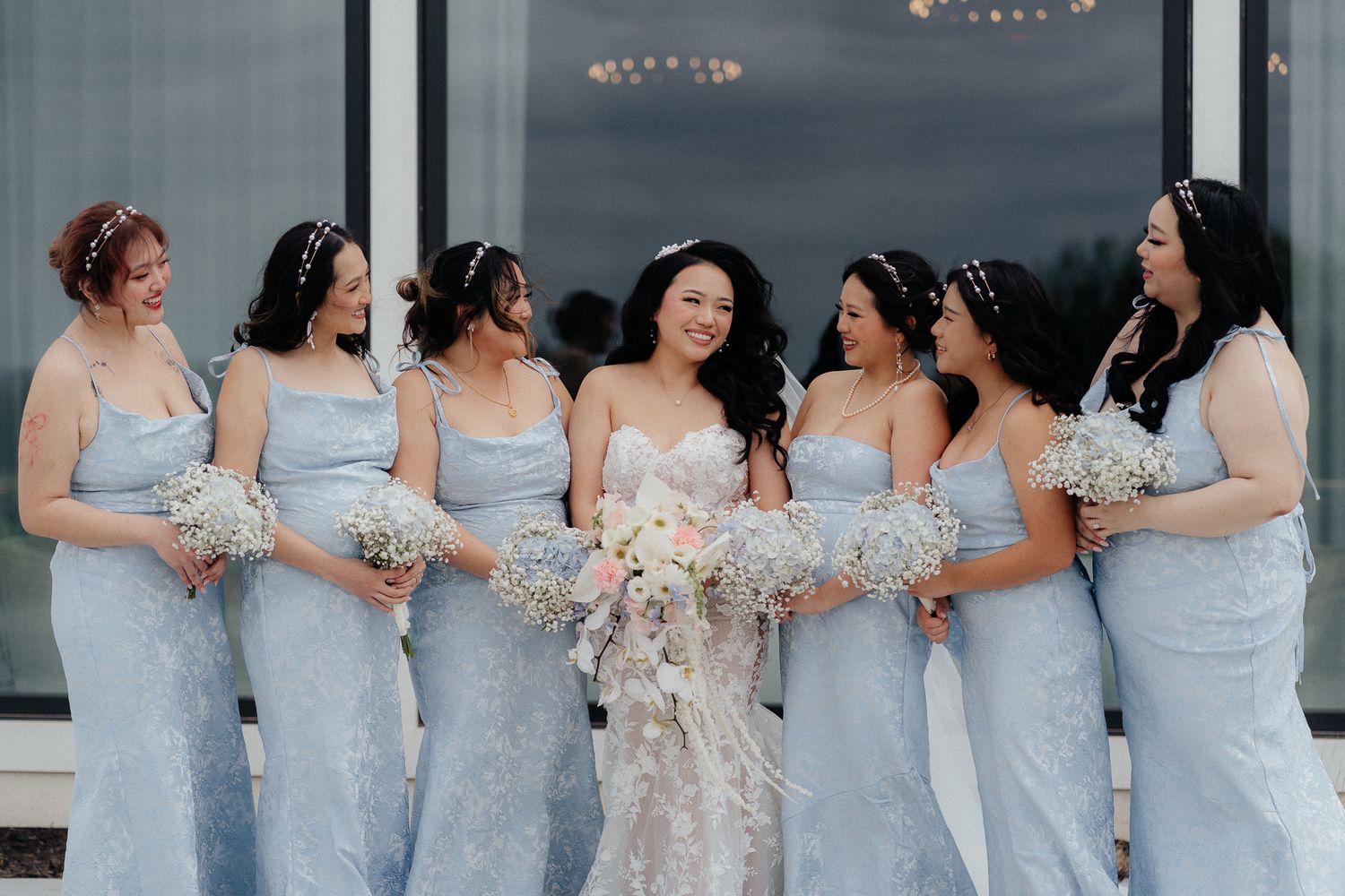 Wedding party in pale blue dresses holding bouquets against white background.