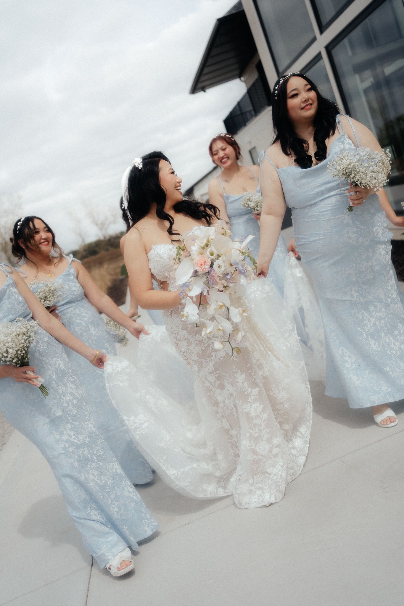 A bridal party poses in light blue bridesmaid dresses alongside a bride in a detailed lace wedding gown.