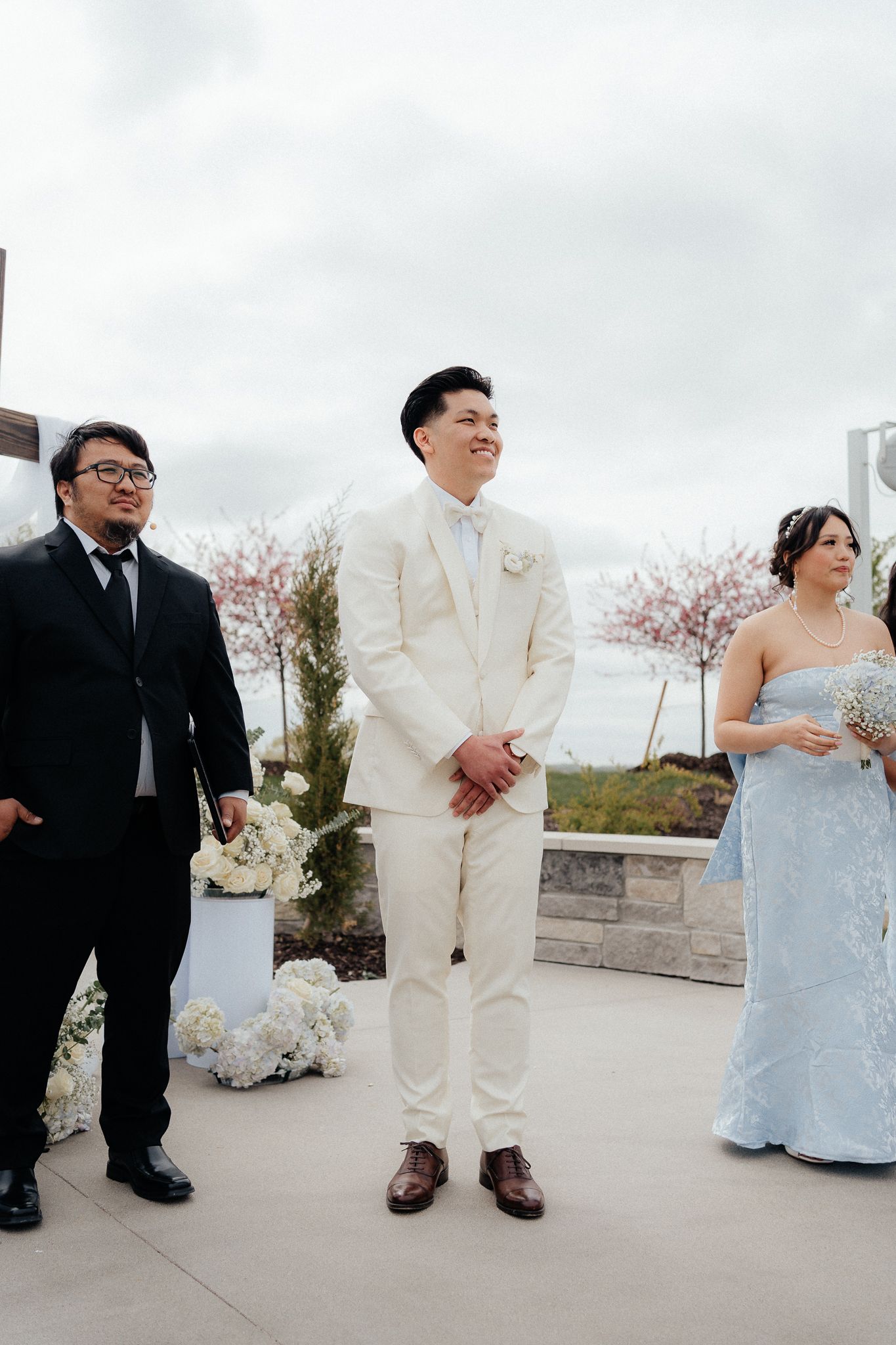 Outdoor wedding ceremony with three people standing at the altar against a cloudy sky with cherry blossoms.