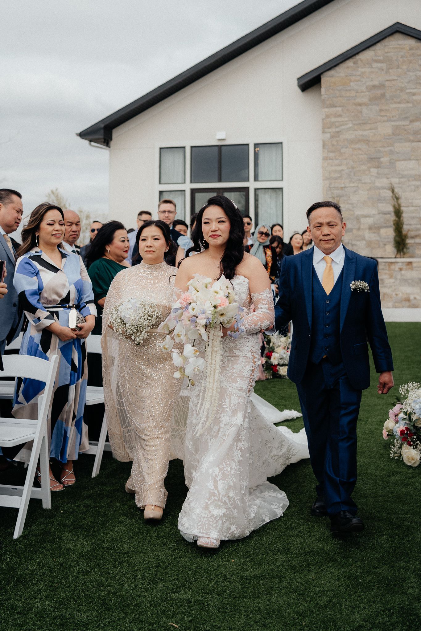 Newlyweds exit their wedding ceremony surrounded by guests on a grassy outdoor venue.