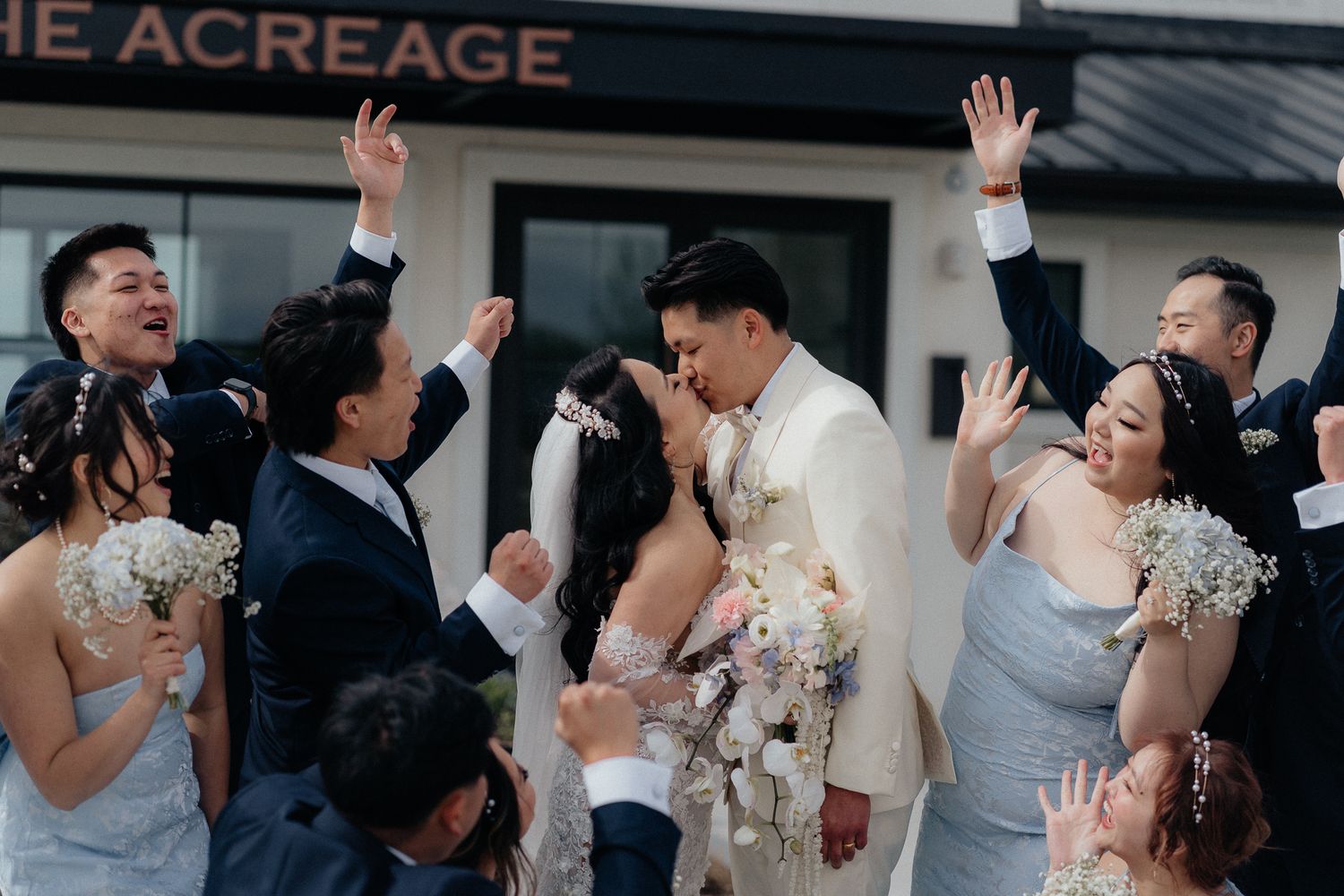 Wedding guests celebrate with raised hands and joyful expressions during an outdoor celebration at The Acreage venue.
