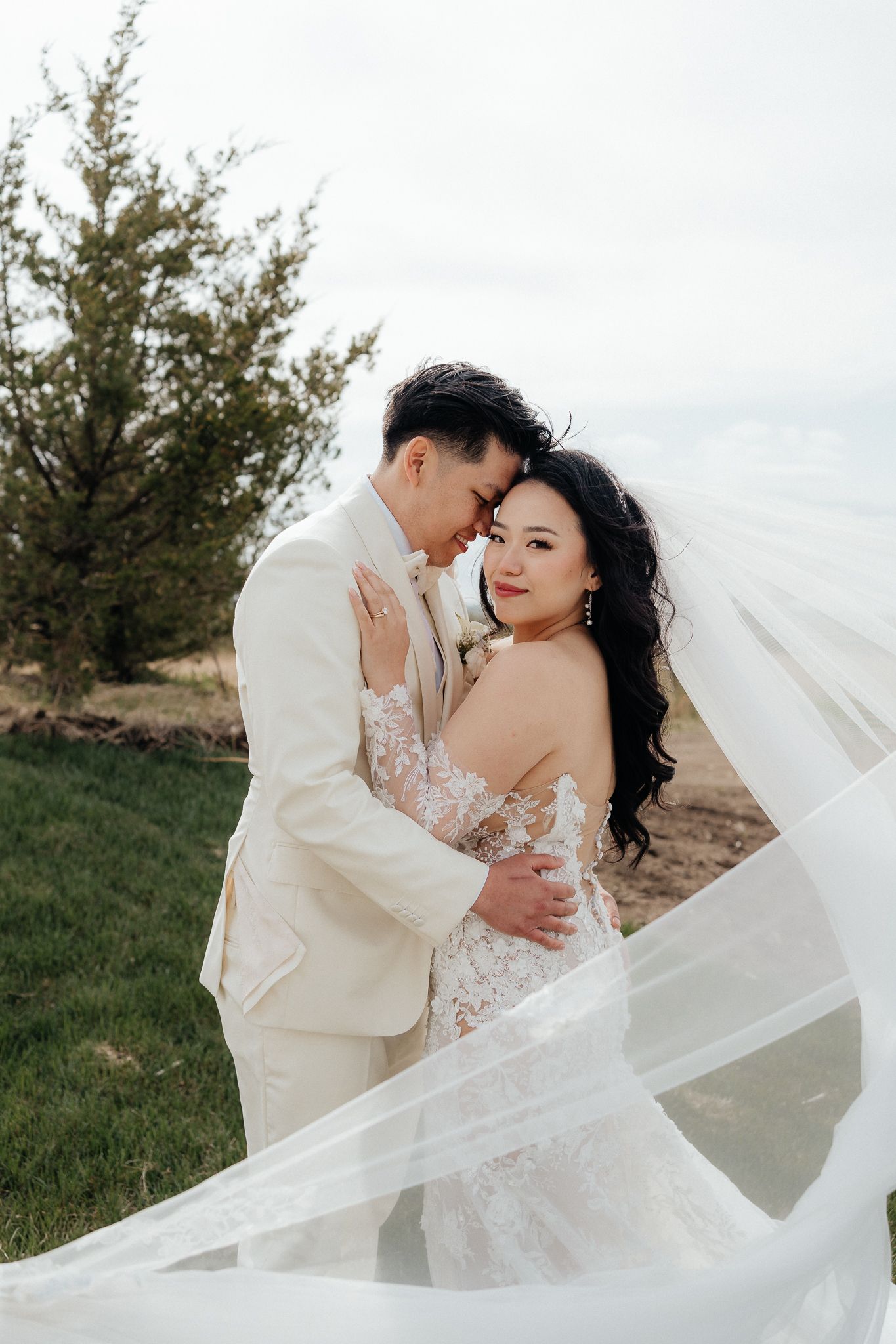 Wedding couple embracing outdoors with flowing veil in the wind.