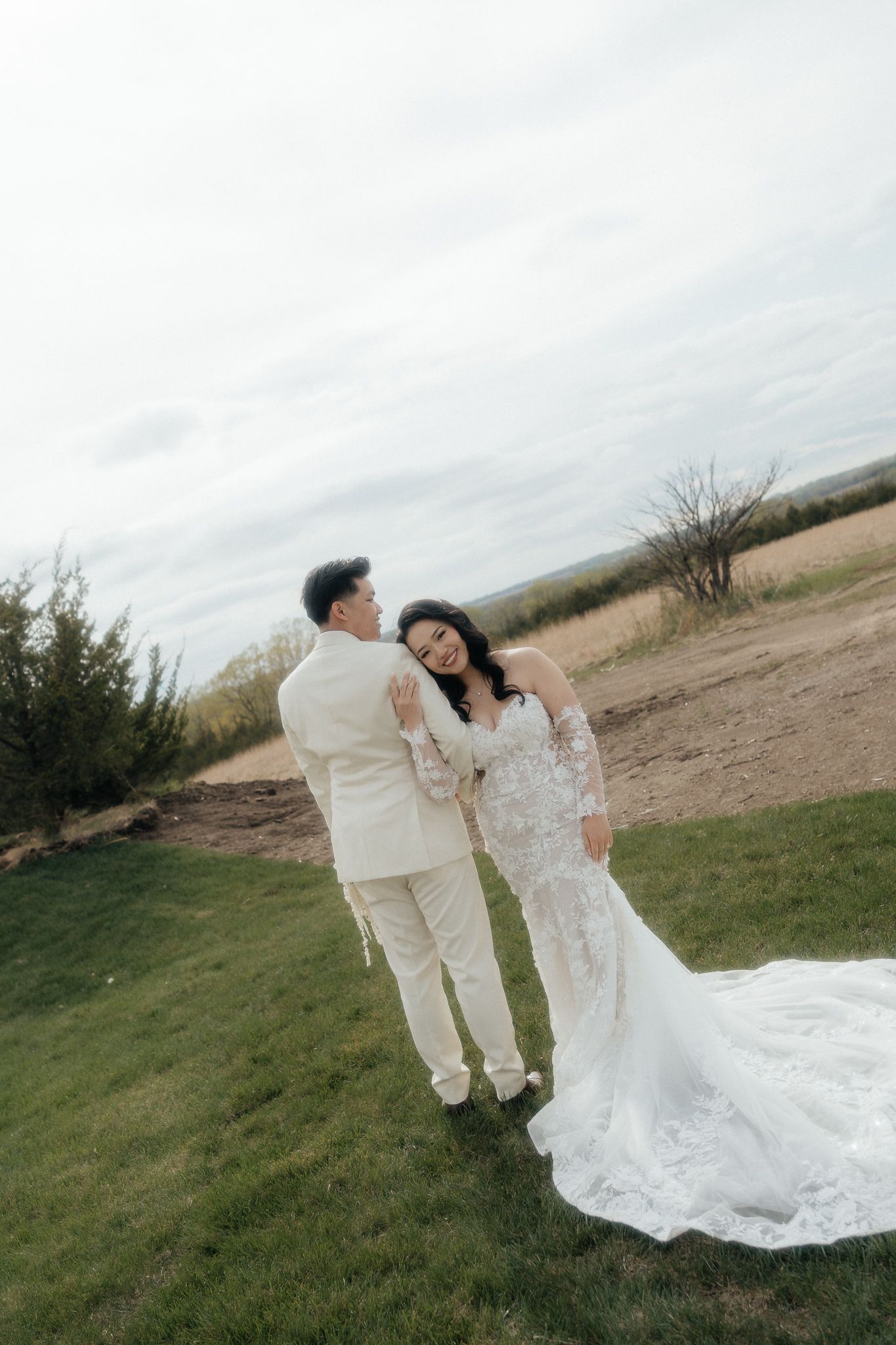 A romantic wedding portrait of a couple in white attire against an outdoor landscape.