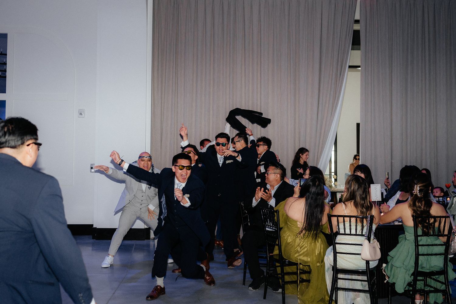 Wedding guests wearing dark outfits and sunglasses pose energetically during a reception celebration.