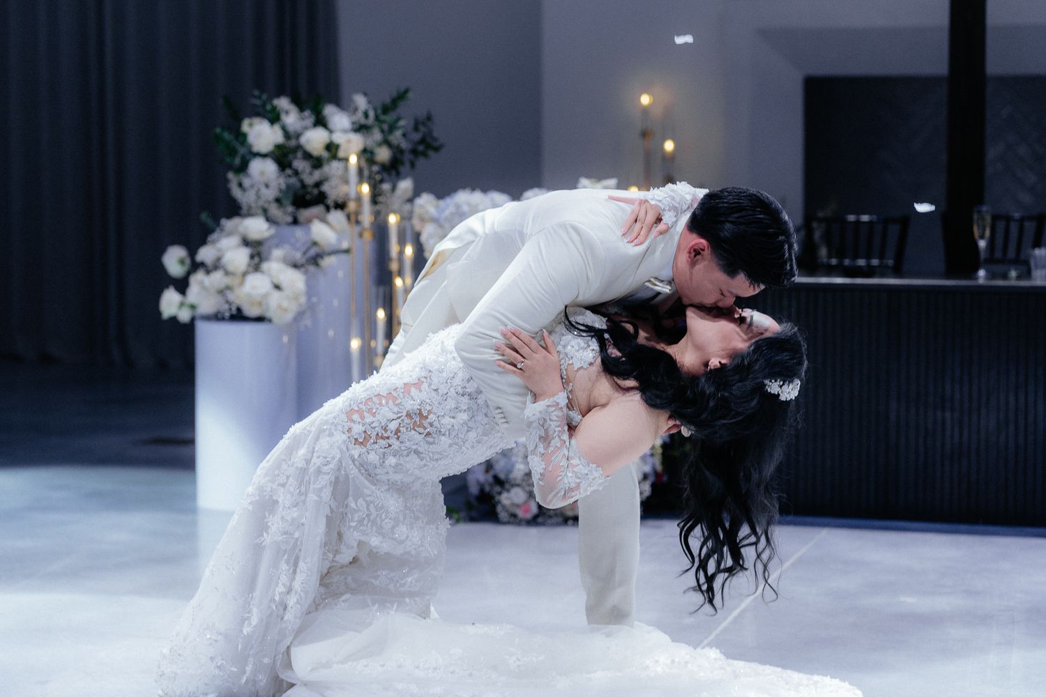 A romantic dip dance between newlyweds on a dance floor with floral decorations and soft lighting.