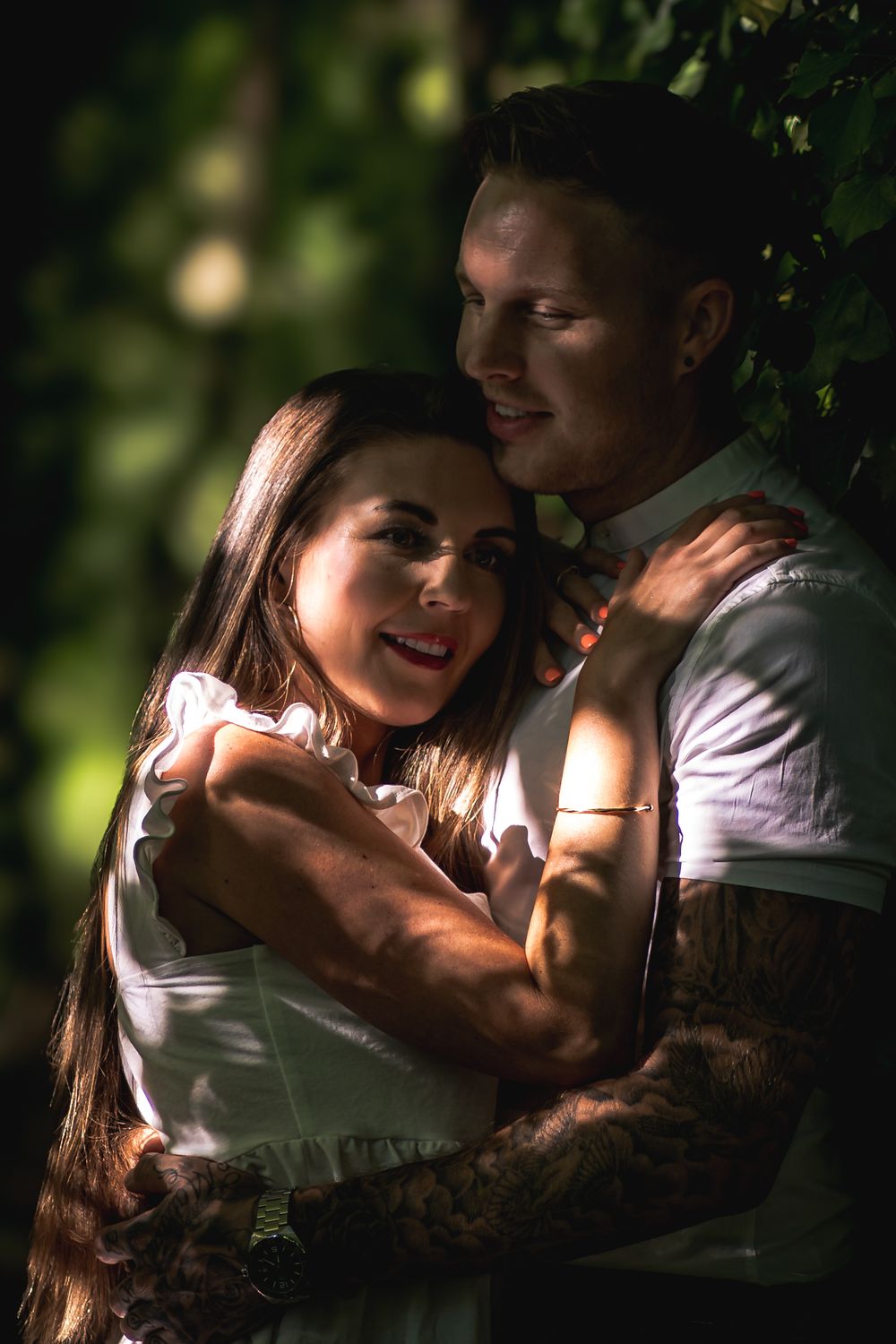 Intimate portrait of couple sharing tender moment in natural lighting among foliage.