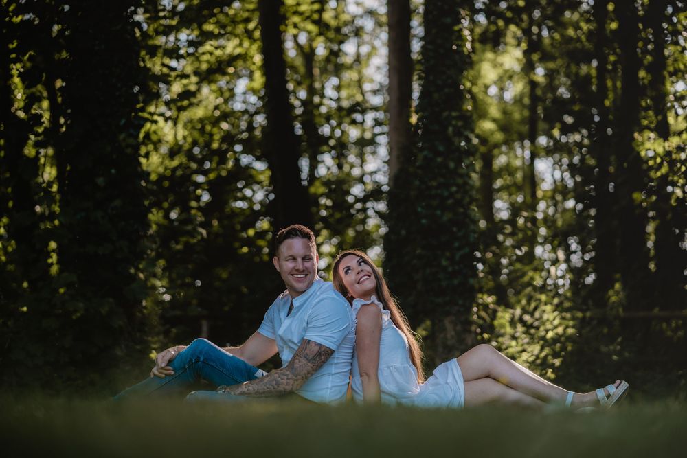 Couple in white clothing relaxing together on grassy forest floor.