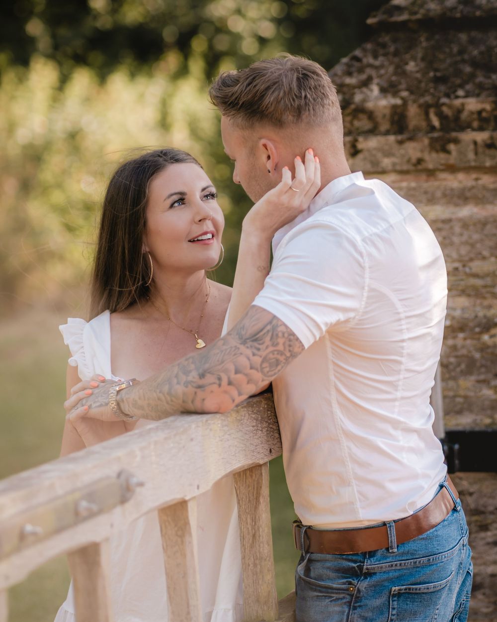 A romantic couple shares an intimate moment by a rustic wooden fence at sunset.