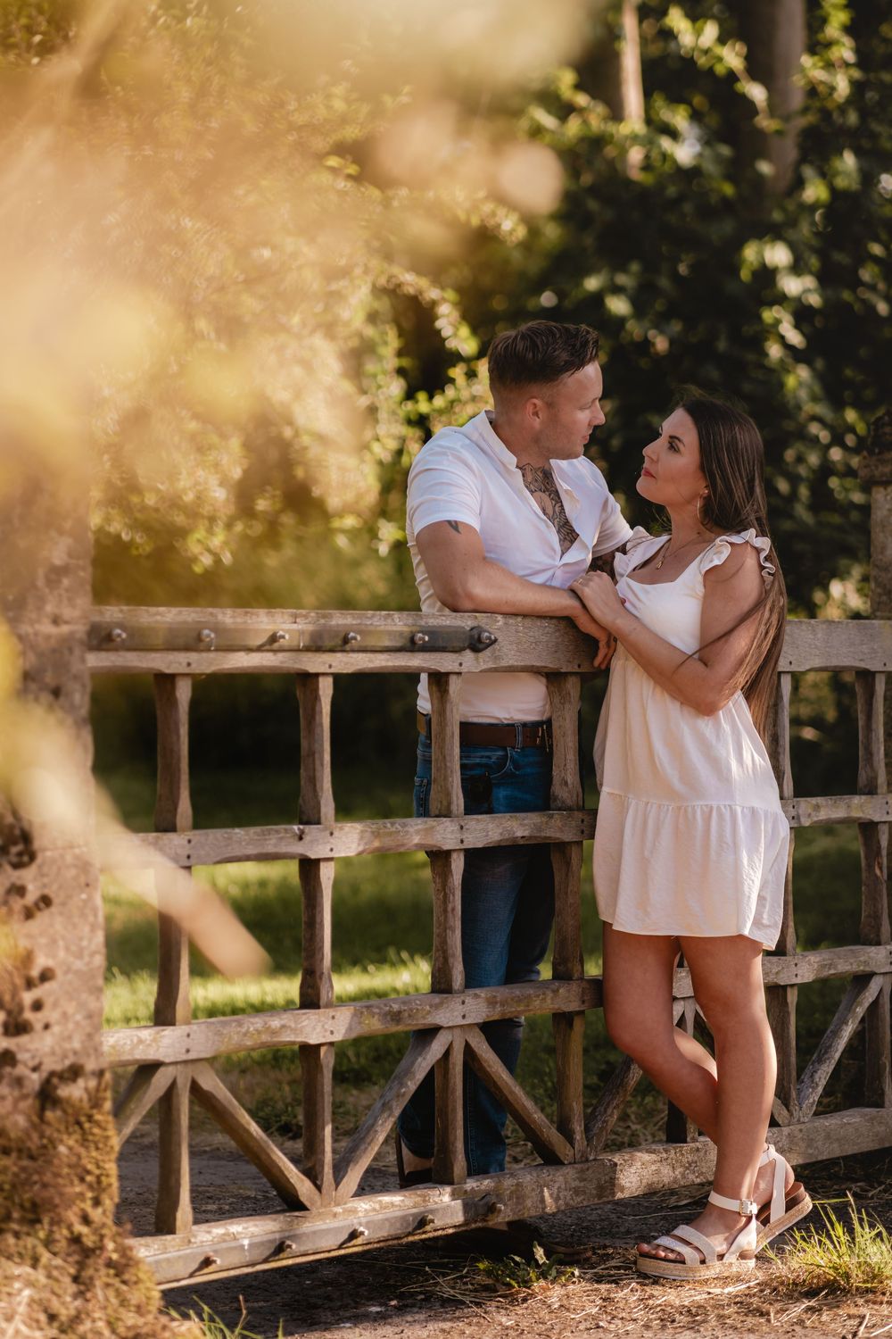 A couple in summer attire embraces on a wooden bridge during golden hour.