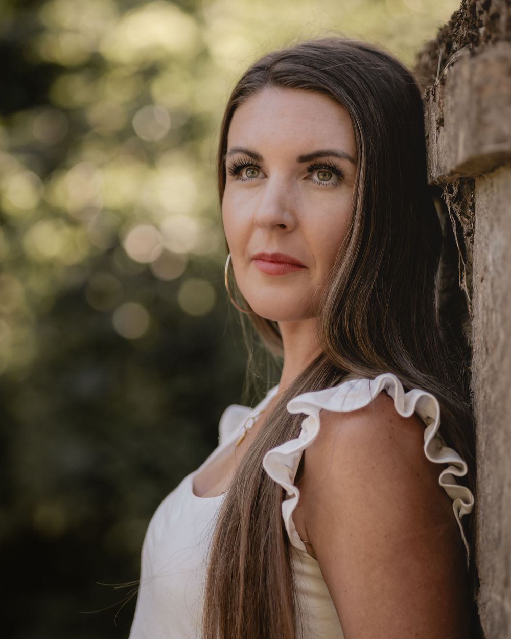 Portrait of a woman in a white summer dress with long dark hair against a bokeh background.