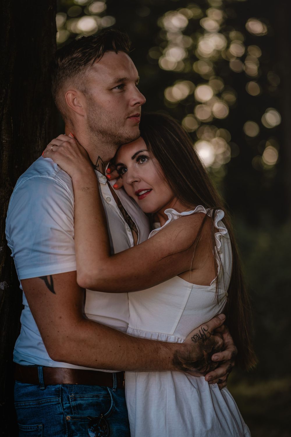 Romantic couple embrace in dramatic lighting with bokeh effect in background.