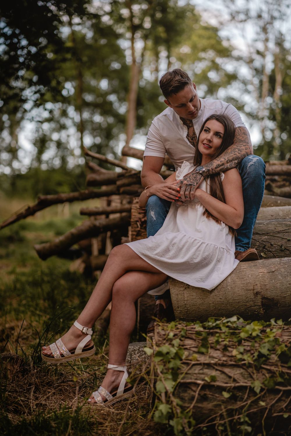 Couple poses on fallen logs during sunset photoshoot in nature.