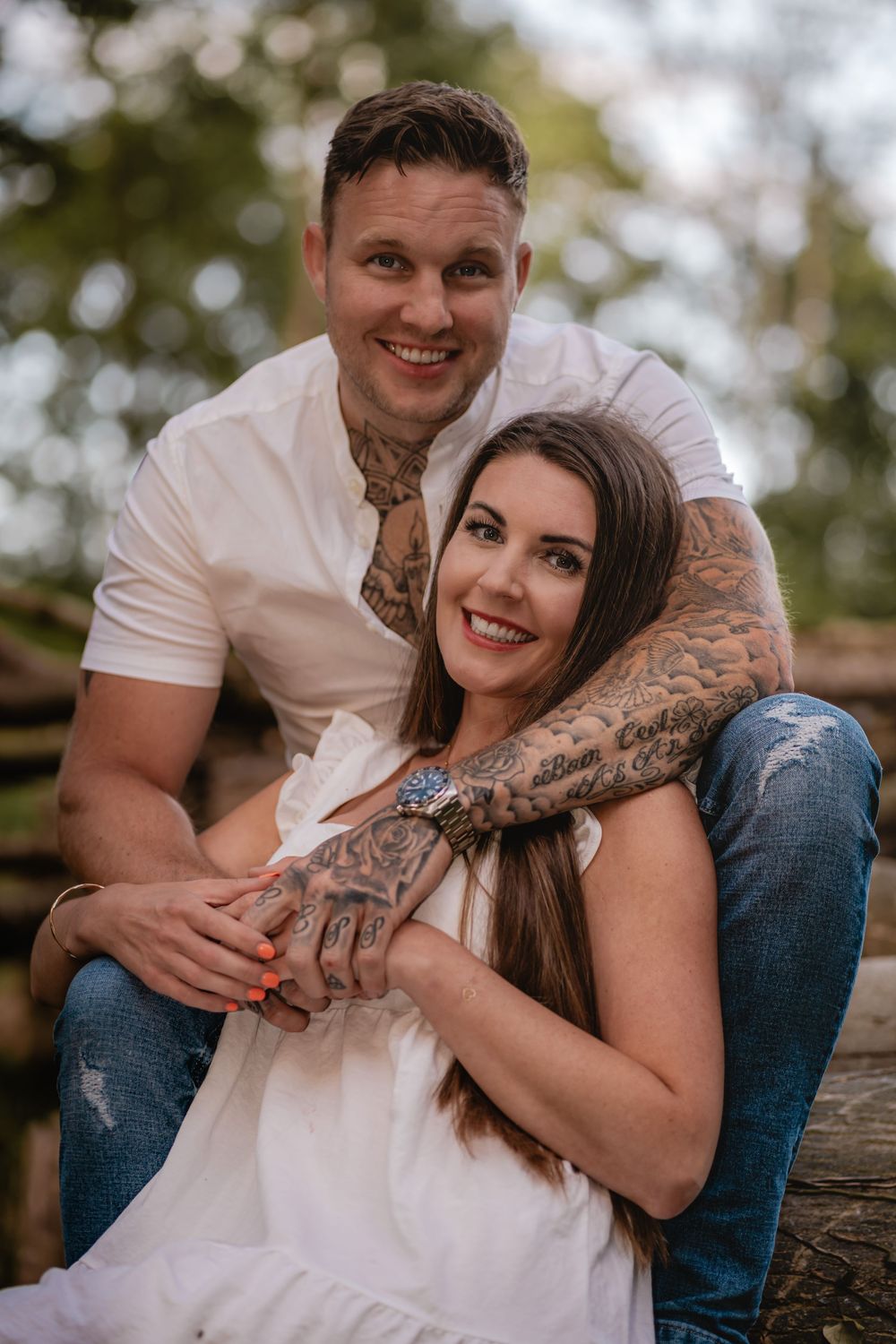 Happy couple sits on rustic log during outdoor photo session.