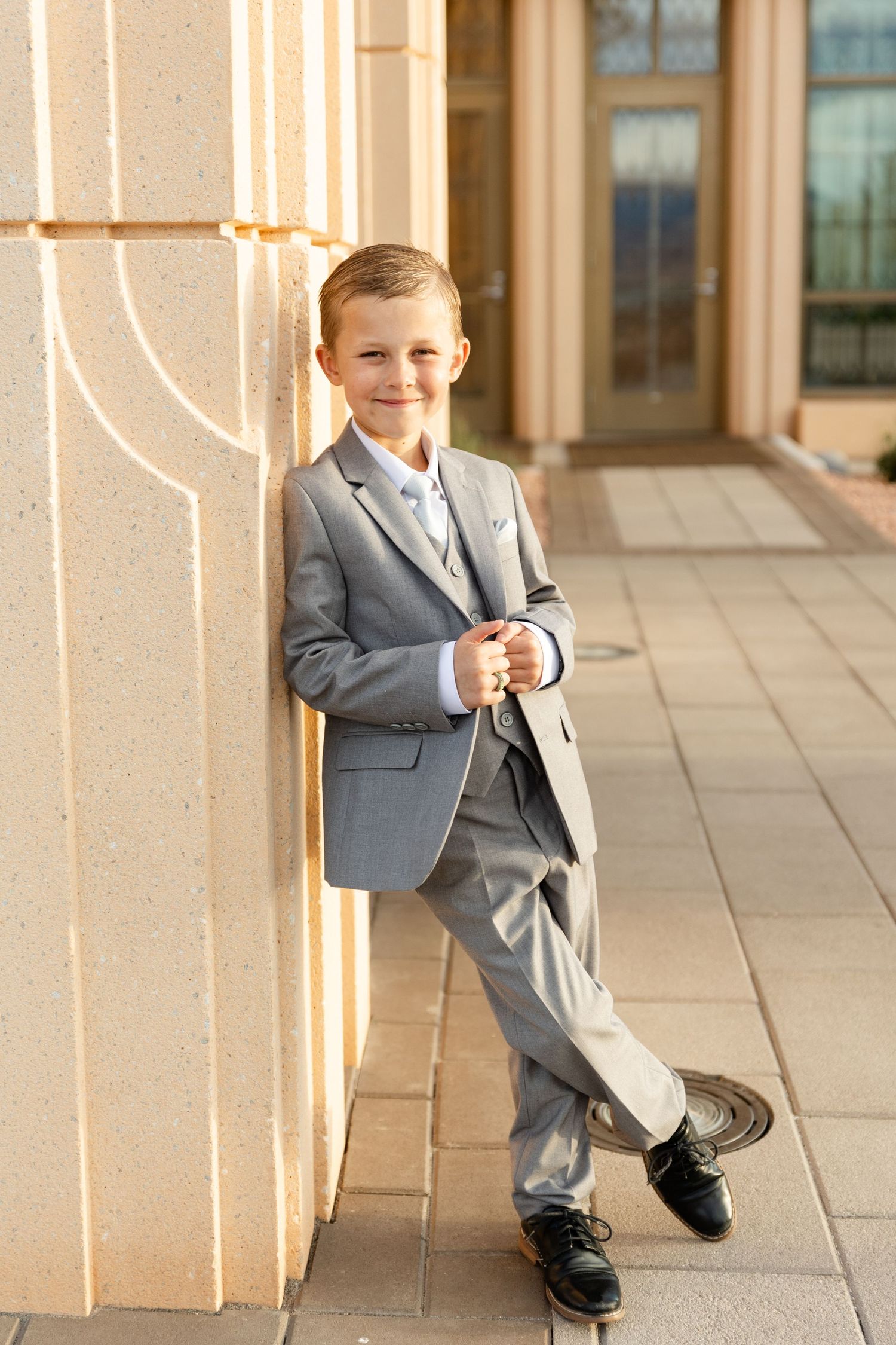 8 year old boy leaning up against the pillar of the temple in a gray suit