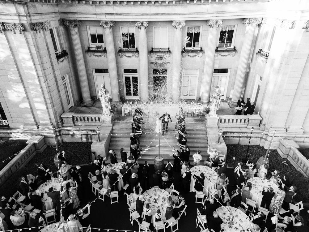 Elegant black and white aerial view of an outdoor wedding reception with guests dining on a grand building terrace.