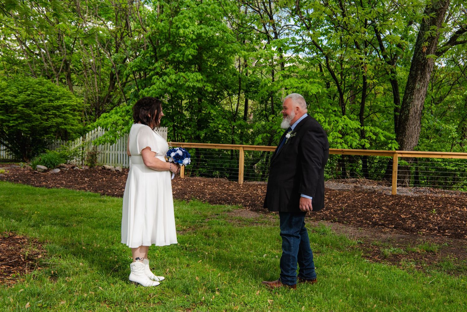 Wedding ceremony in progress under a wooden arch surrounded by lush greenery.