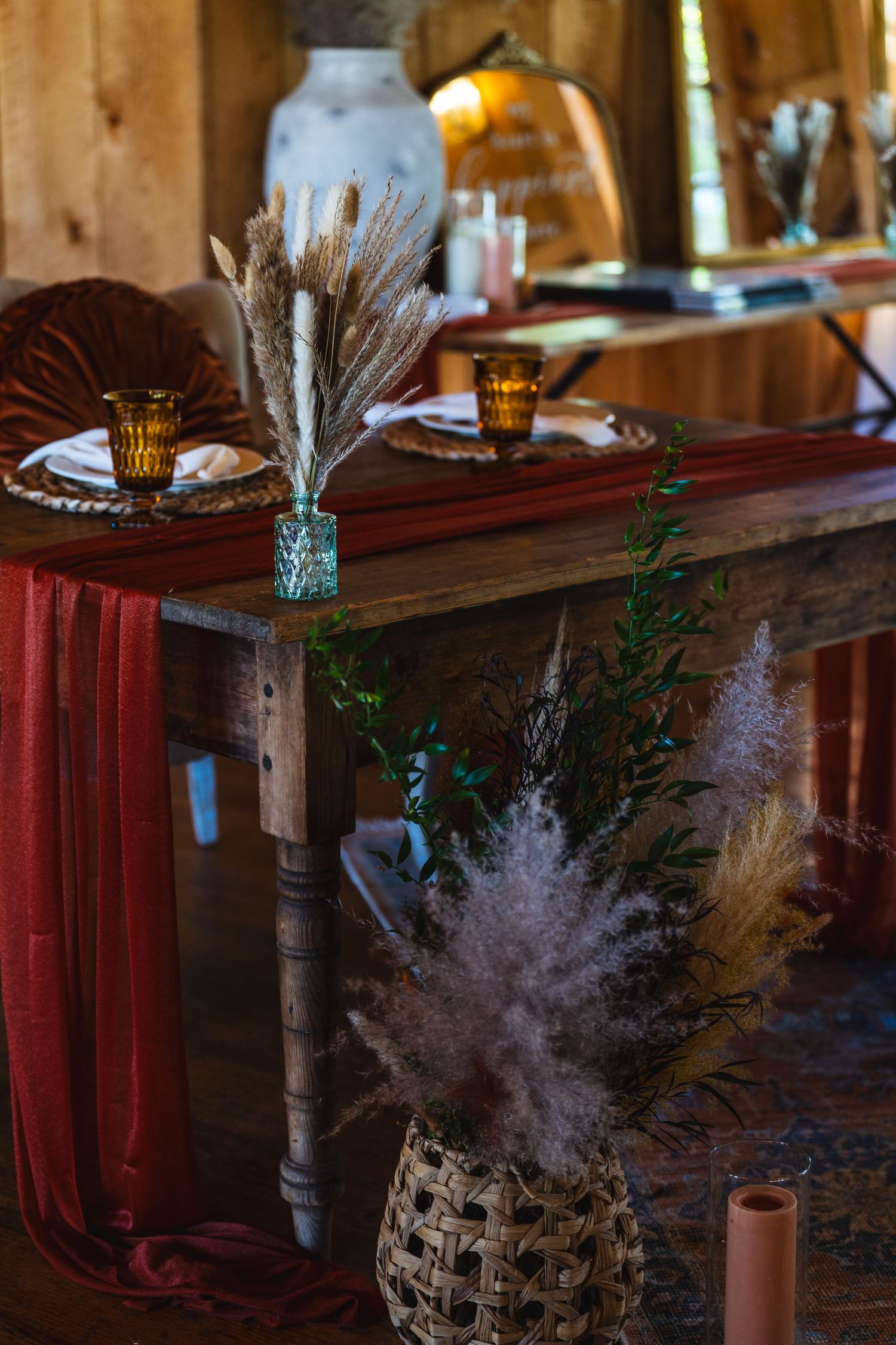 Rustic home decor with dried grasses in vases, warm candlelight, and red drapery on wooden furniture in cozy interior setting.
