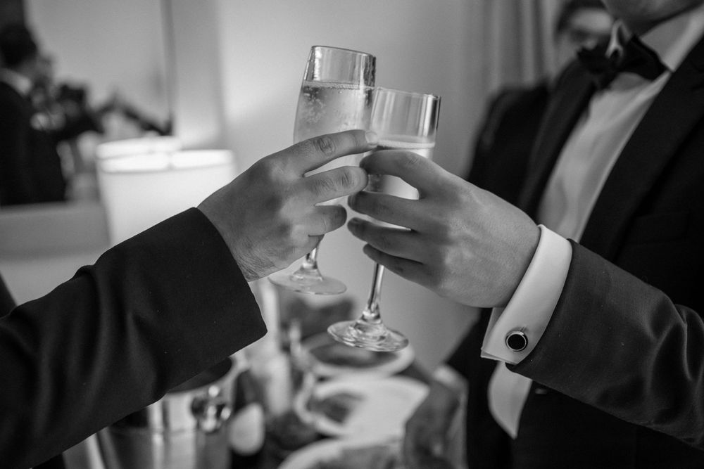 Two hands in formal attire clink champagne glasses together in an elegant black and white wedding celebration toast.