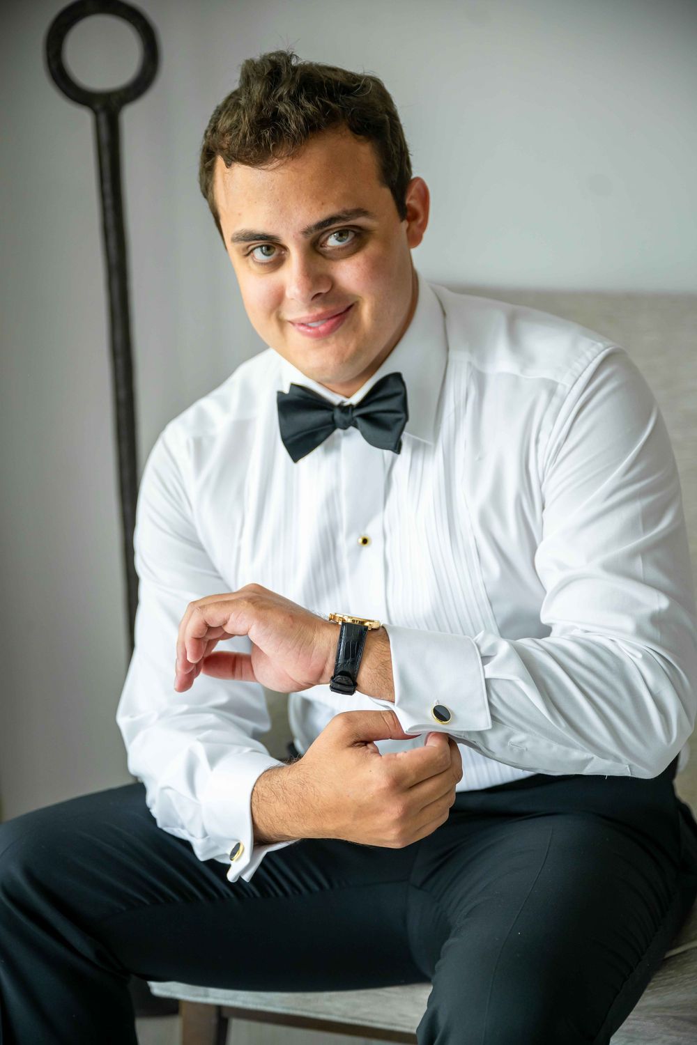 Someone adjusts their cufflinks while wearing a classic white dress shirt and black bow tie during formal preparation.