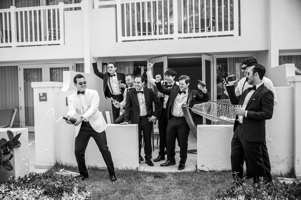 Black and white photo showing a celebratory group in formal attire posing playfully outside a building with white railings.