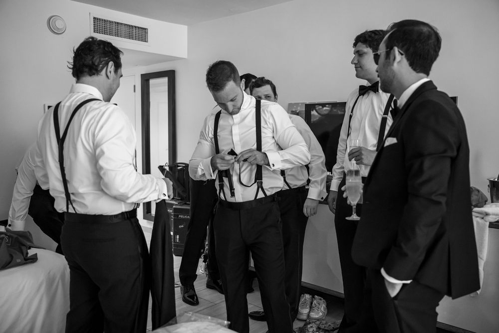 A group of formally dressed people in black and white attire gather in conversation in a hotel room.