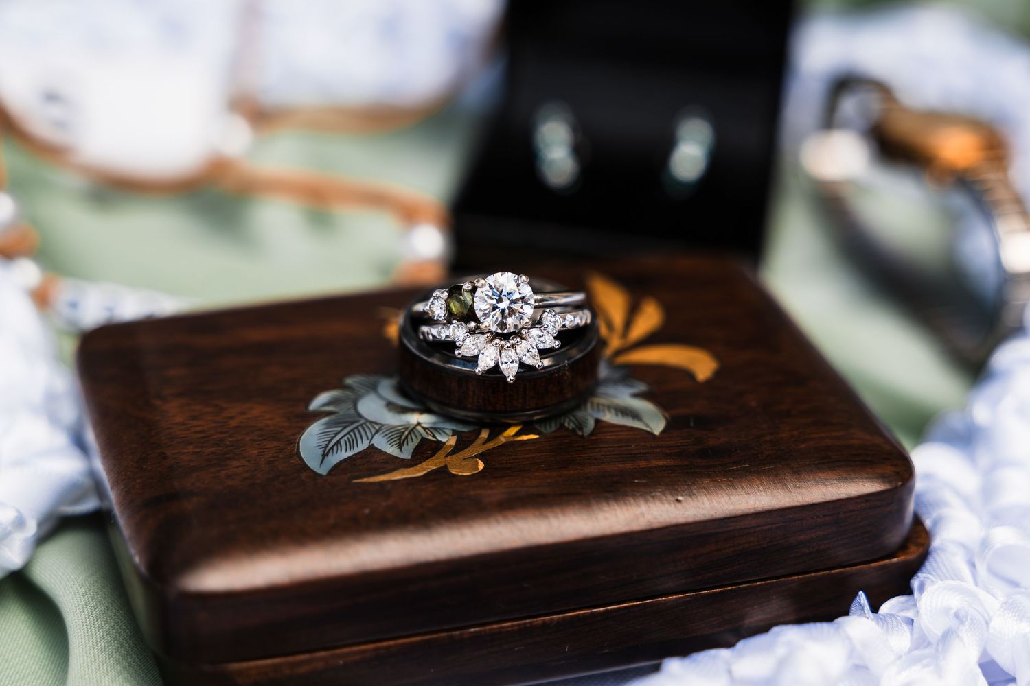 Wedding rings displayed on a dark brown wooden box with decorative floral elements and soft green accents.