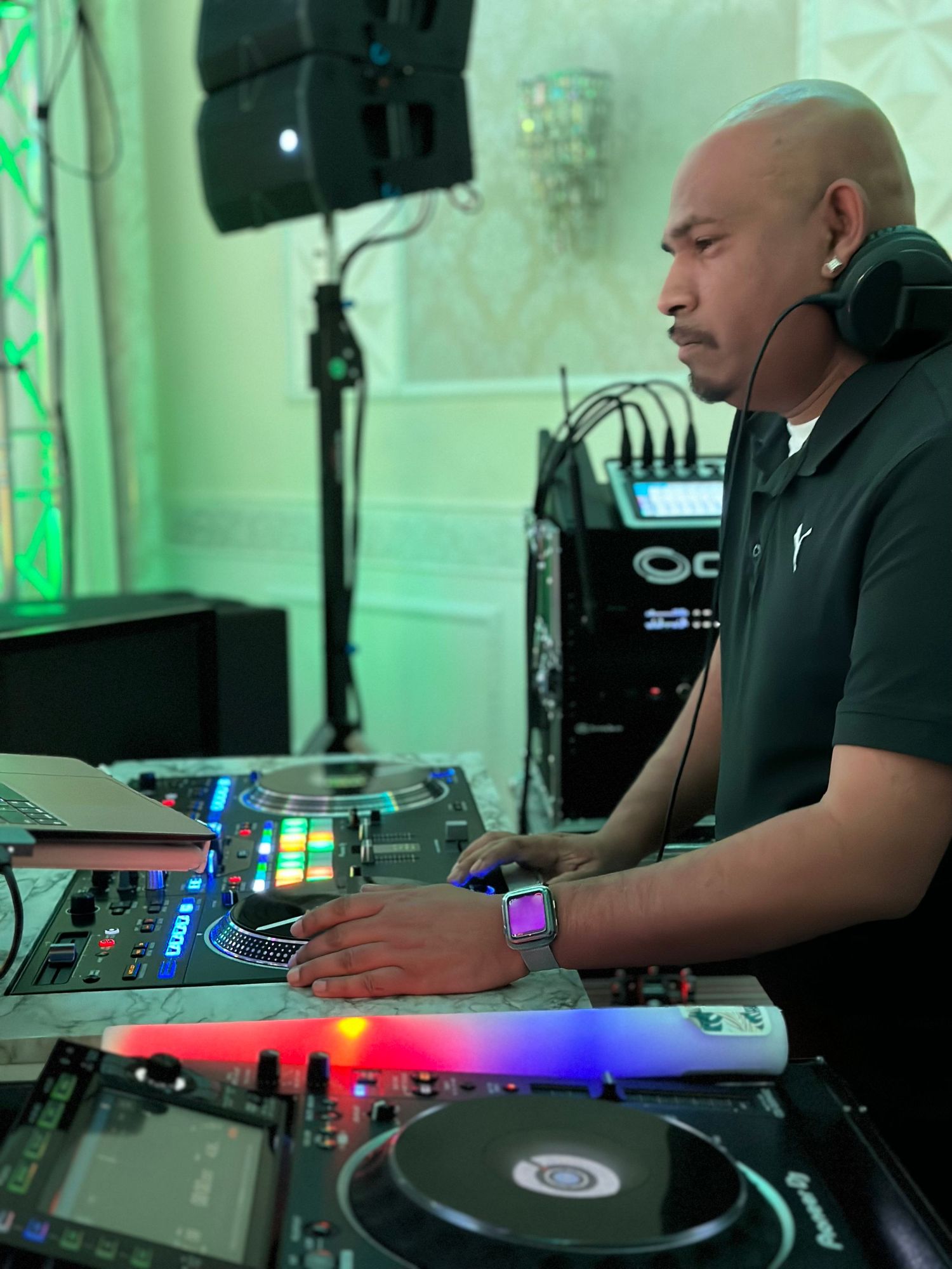 A DJ performs at an event with professional equipment including turntables and mixers under green lighting.
