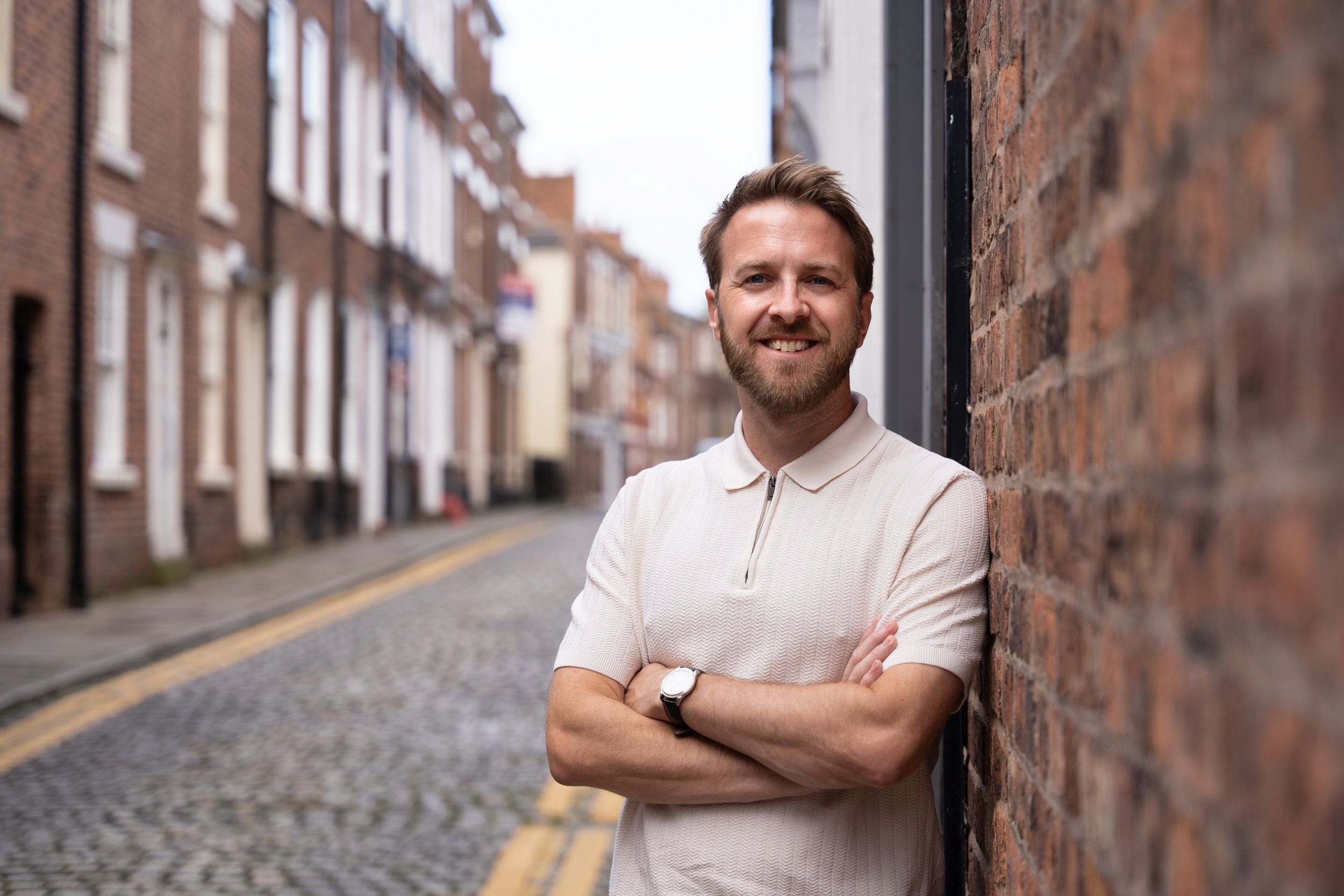 Life coach leans on a brick wall during a personal branding photoshoot for men