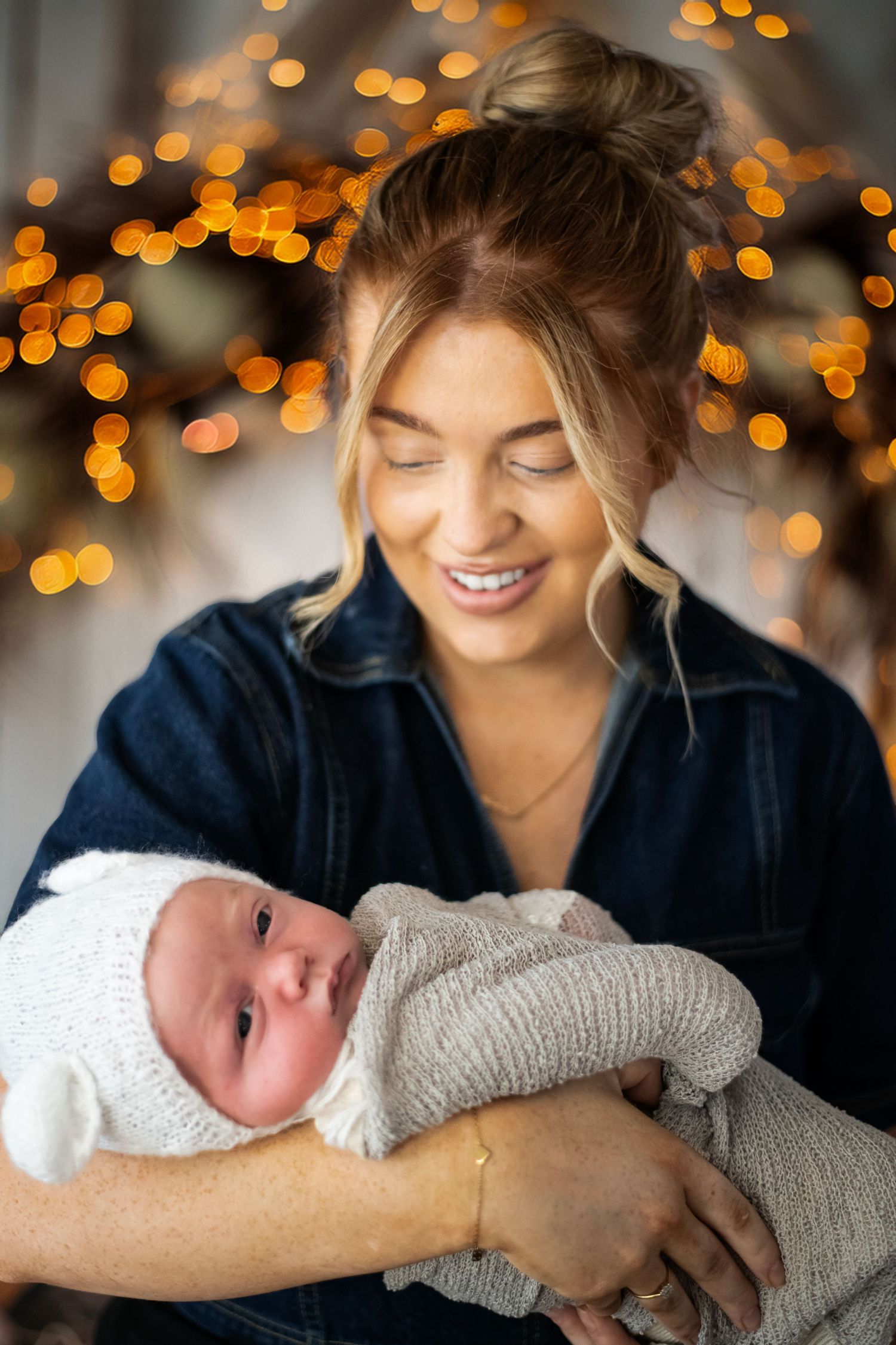 A loving moment captured with a baby wrapped in cozy knits against a background of warm holiday lights and bokeh.