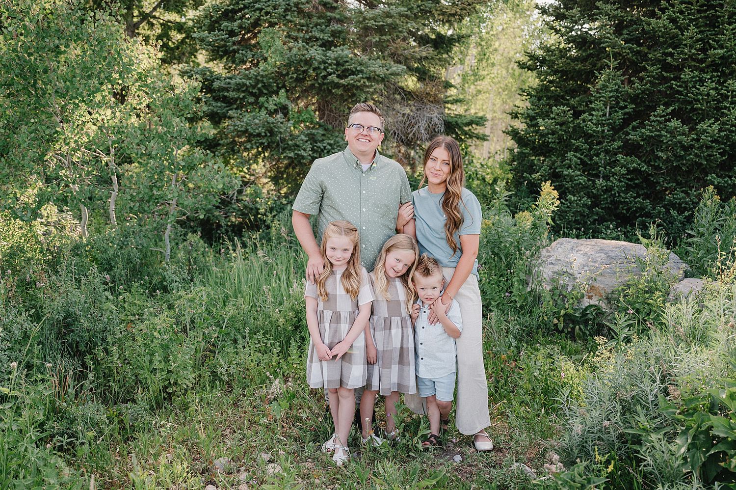 Family gathering poses together outside in a green summer garden setting with coordinated pastel colored outfits.