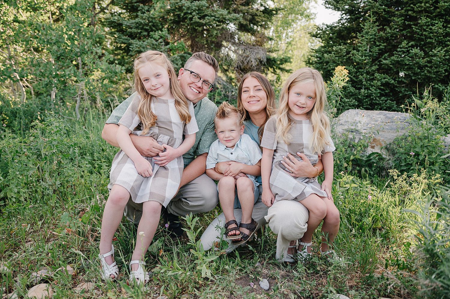 Four casual outdoor family portraits sitting on natural stone steps amid green foliage in a garden setting.