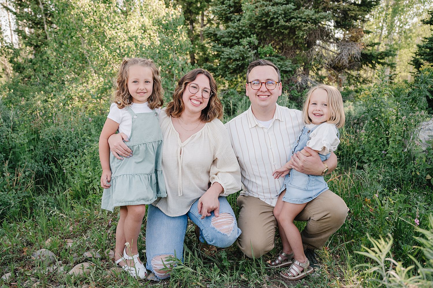 Family in light blue and beige clothing poses together outdoors in a natural green setting during springtime photoshoot.