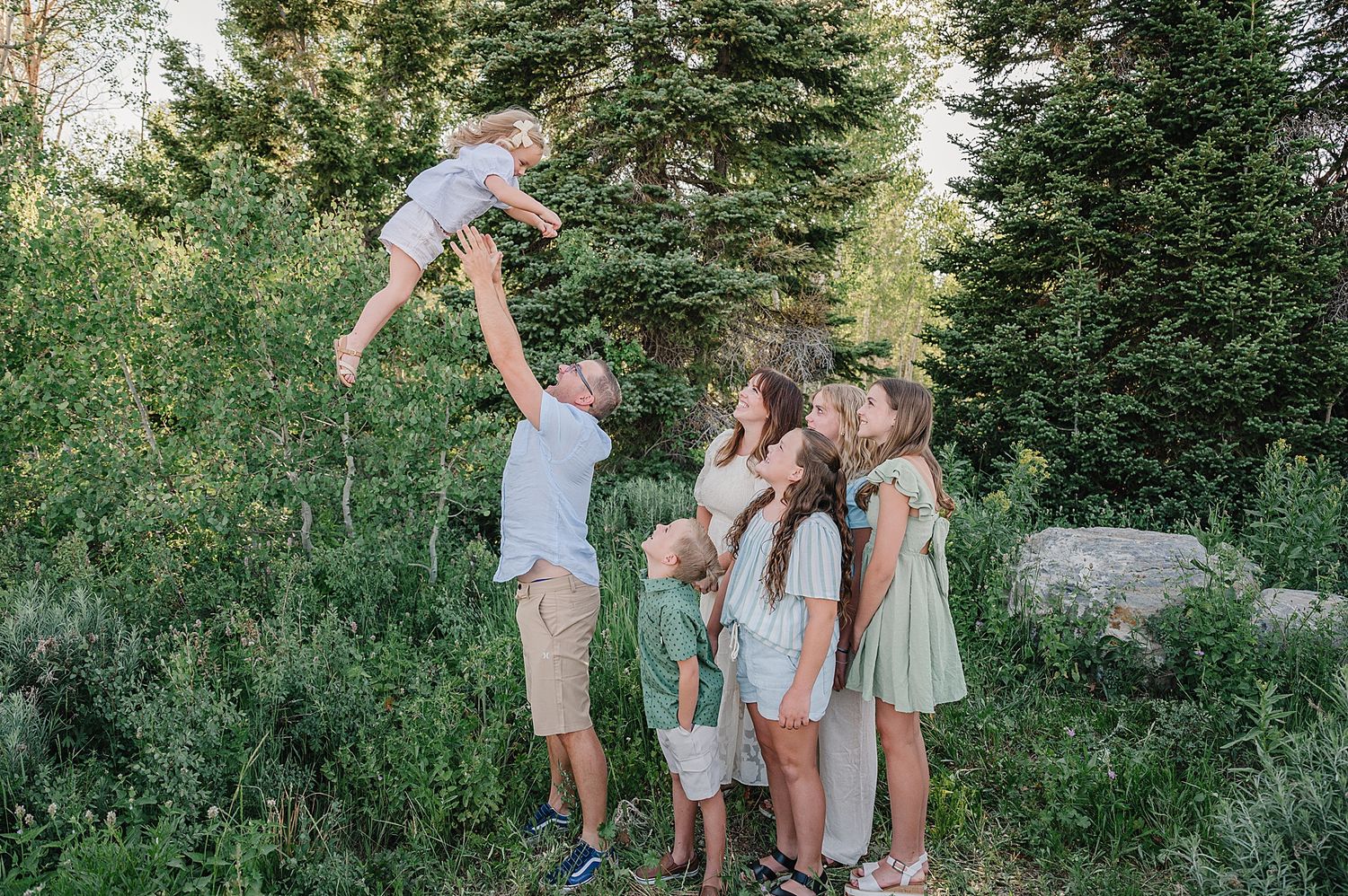 A group stands together in a scenic mountain meadow surrounded by evergreen trees during golden hour.