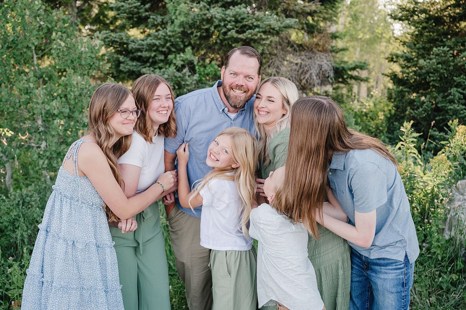 A joyful family shares a candid laughing moment together outdoors surrounded by green foliage in summer.