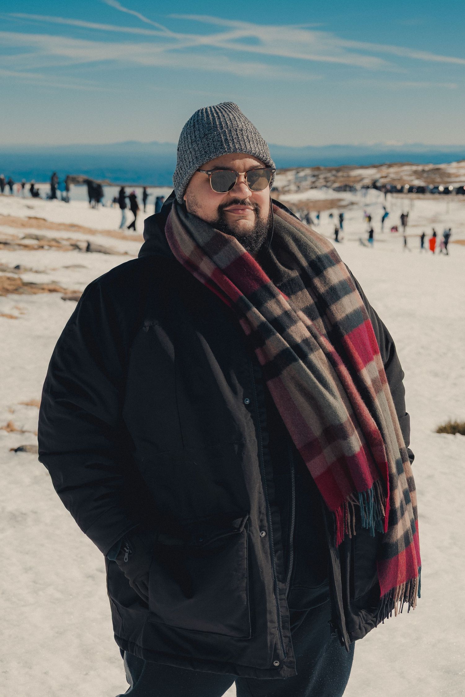 Winter beach portraits with plaid scarf and knit beanie against bright sandy backdrop.