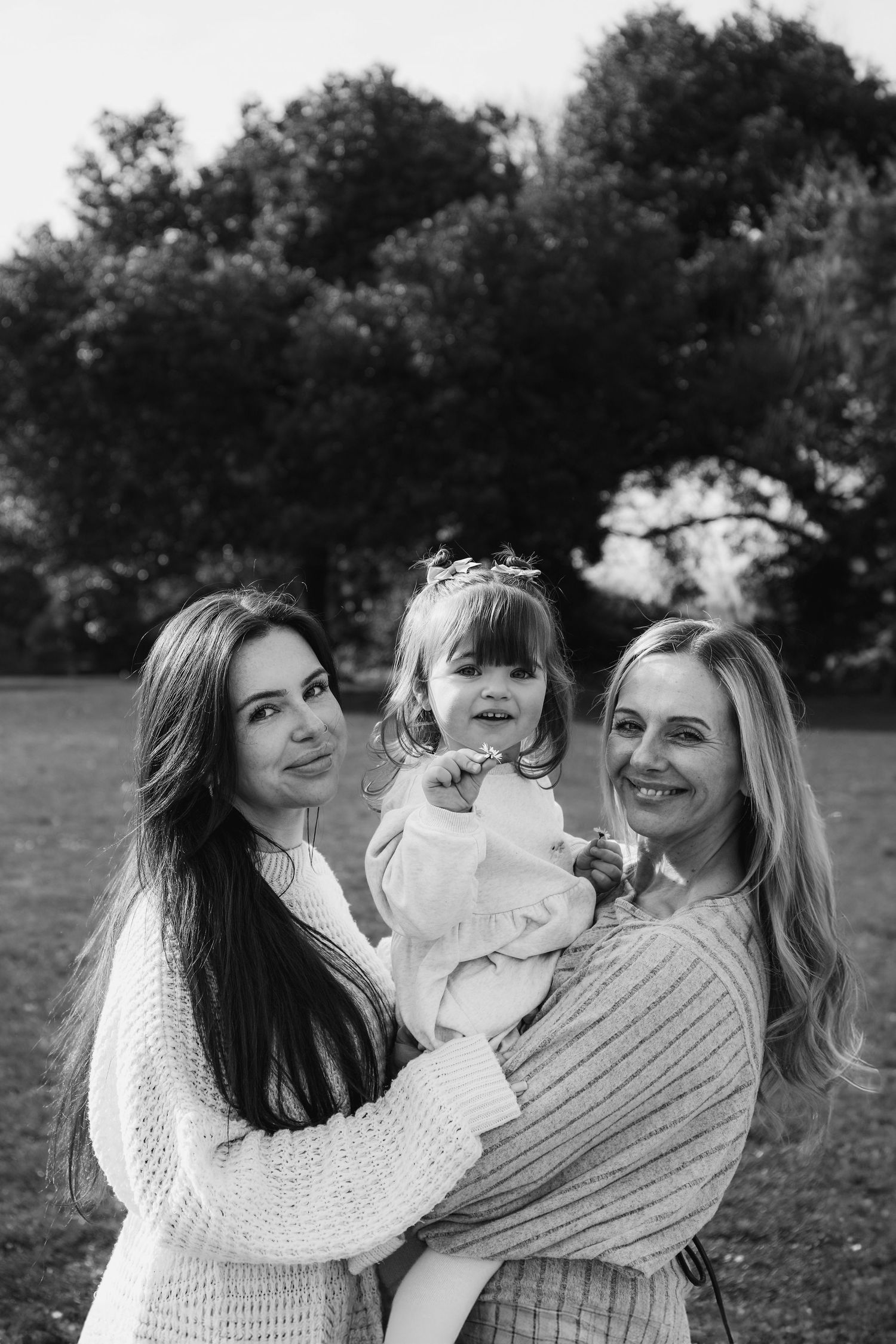 Black and white portrait of three people in cozy sweaters standing together outdoors with trees in background,  family shoot Nottingham