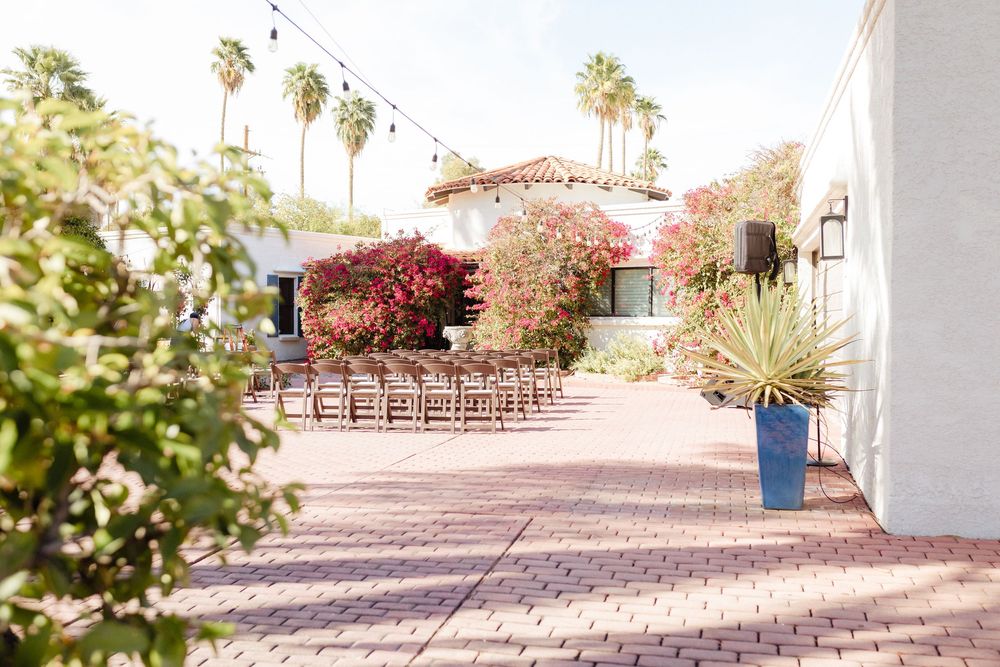 Spanish-style courtyard with red brick pathway, palm trees, and Mediterranean architecture in warm sunlight.