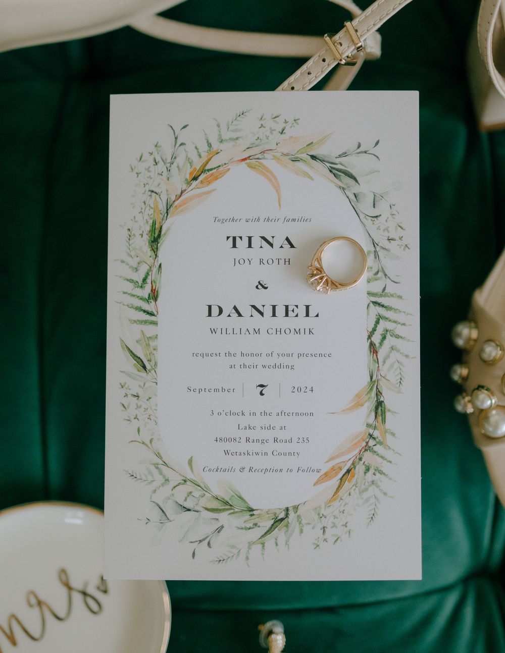 Wedding invitation with watercolor botanical design and wedding rings on an emerald green velvet fabric background.