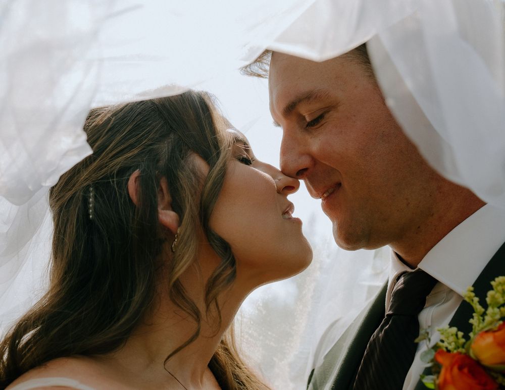 A couple shares a romantic moment during their wedding, with sunlight filtering through white fabric behind them.