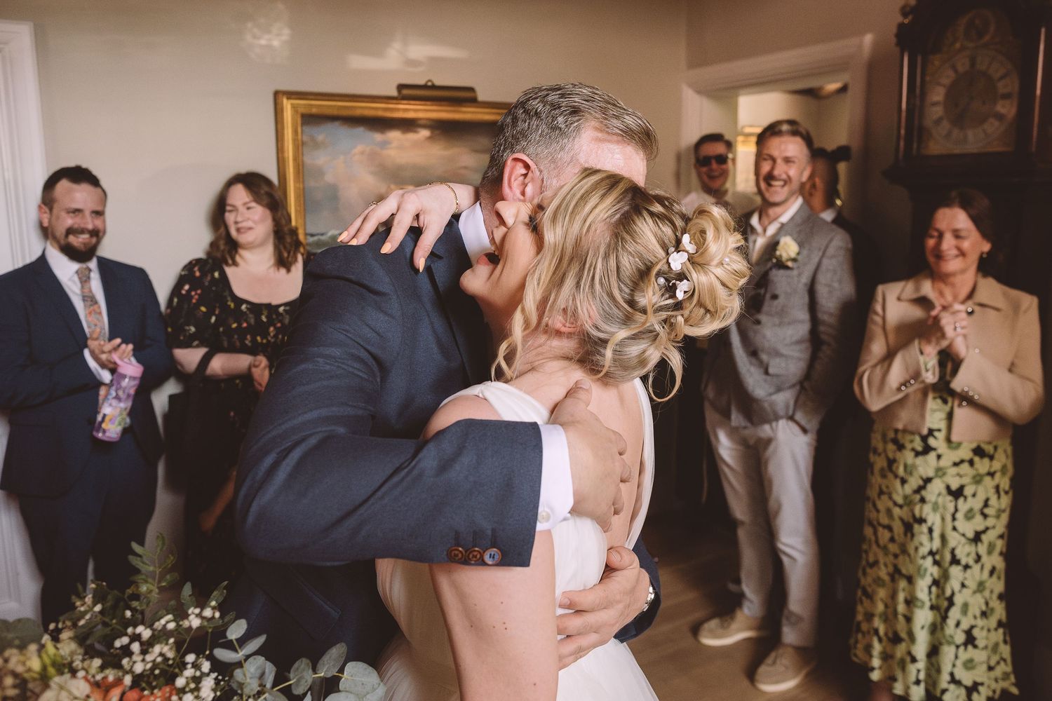 Wedding guests cheer and applaud as newlyweds share a romantic kiss during their intimate indoor celebration.