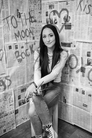 Stylist poses in casual wear against wall covered in rock music posters and graffiti in black and white photo.