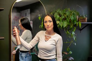 Stylist checking reflection in salon mirror with plants in background.