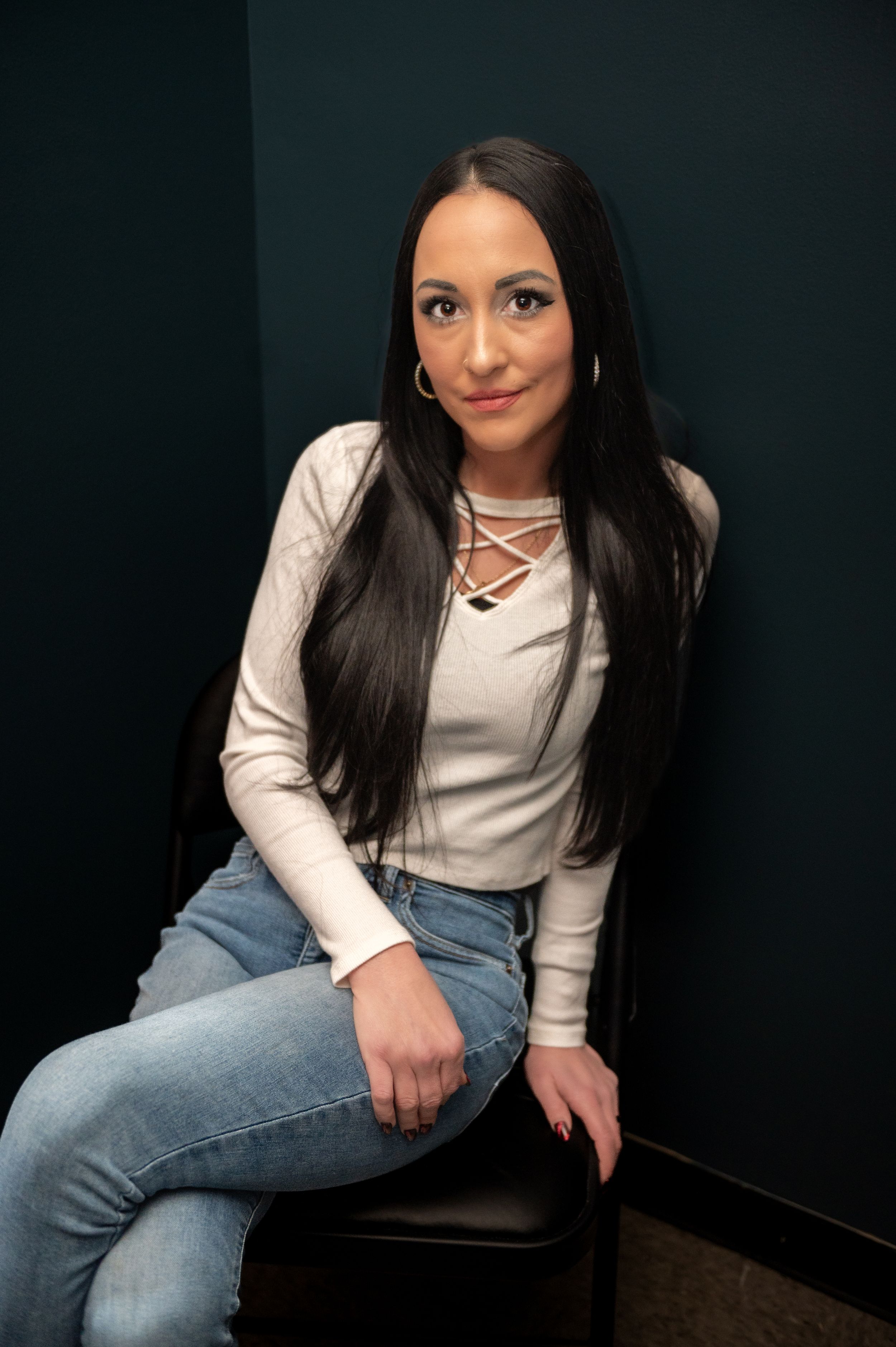 Stylist in white top and jeans poses in professional salon chair.