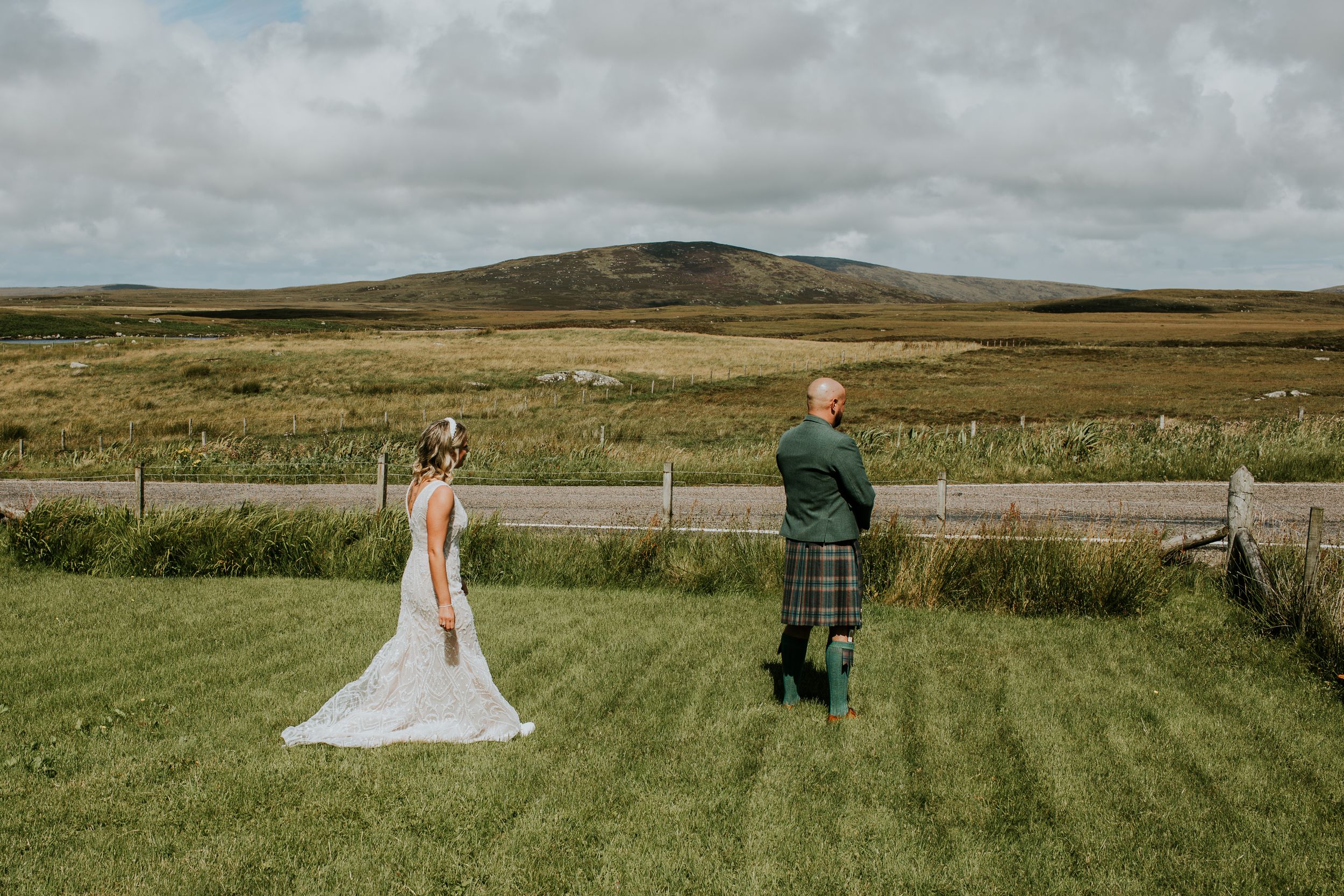 Two people stand in a green field with rolling hills and cloudy skies in the Scottish countryside.