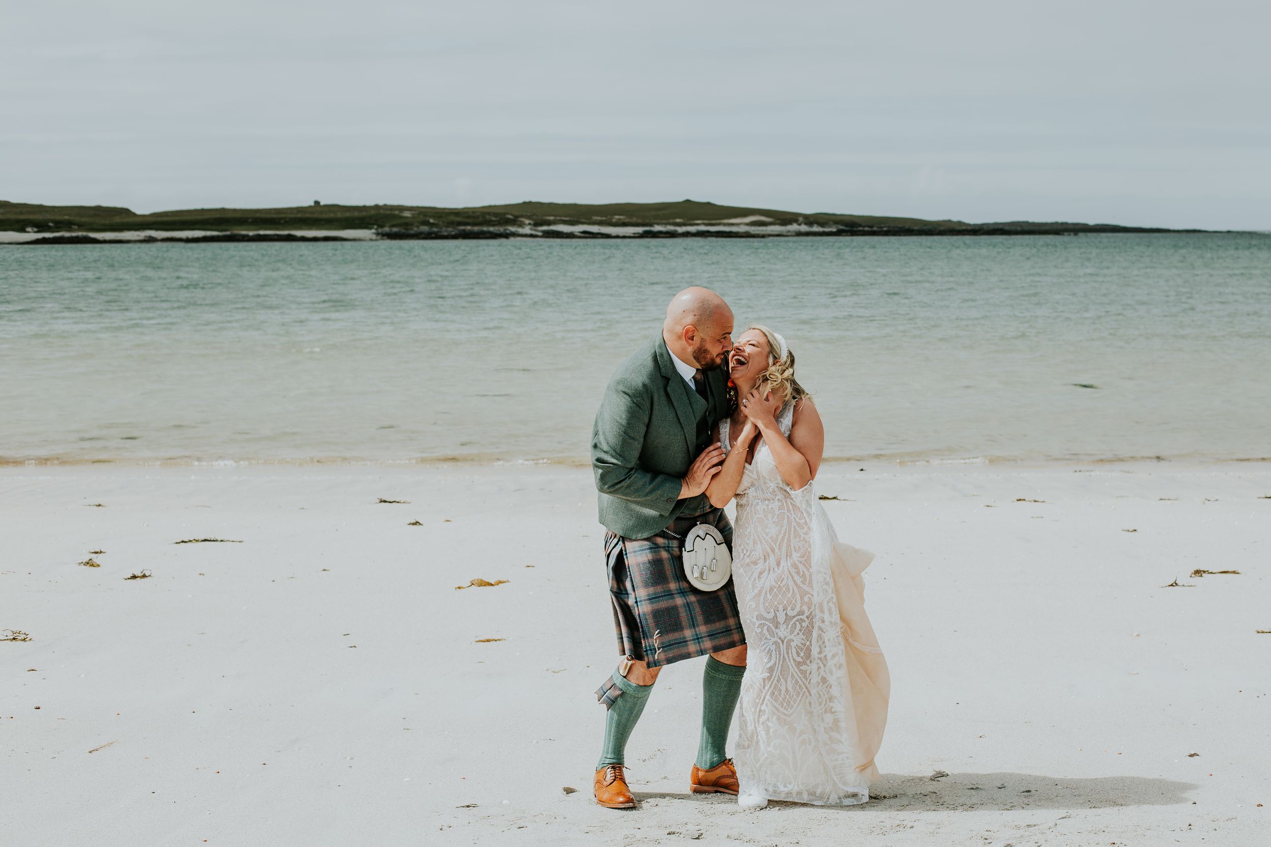 Wedding couple sharing intimate moment on beach with dramatic coastal backdrop.