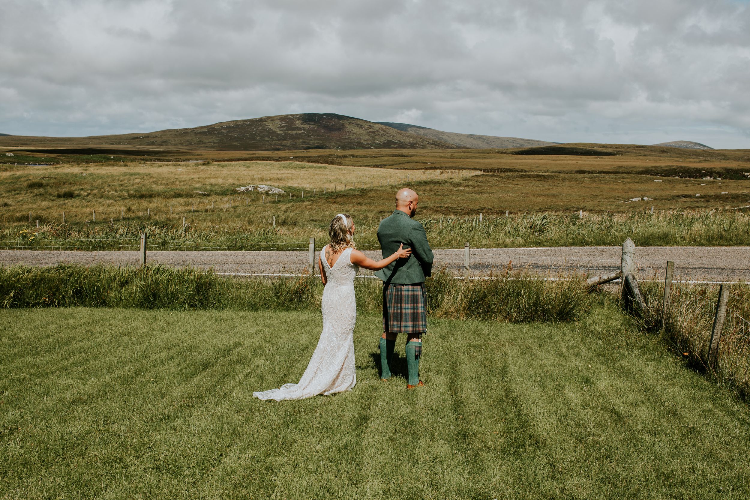 A wedding couple stands in the Scottish countryside with rolling hills and grasslands in the background.