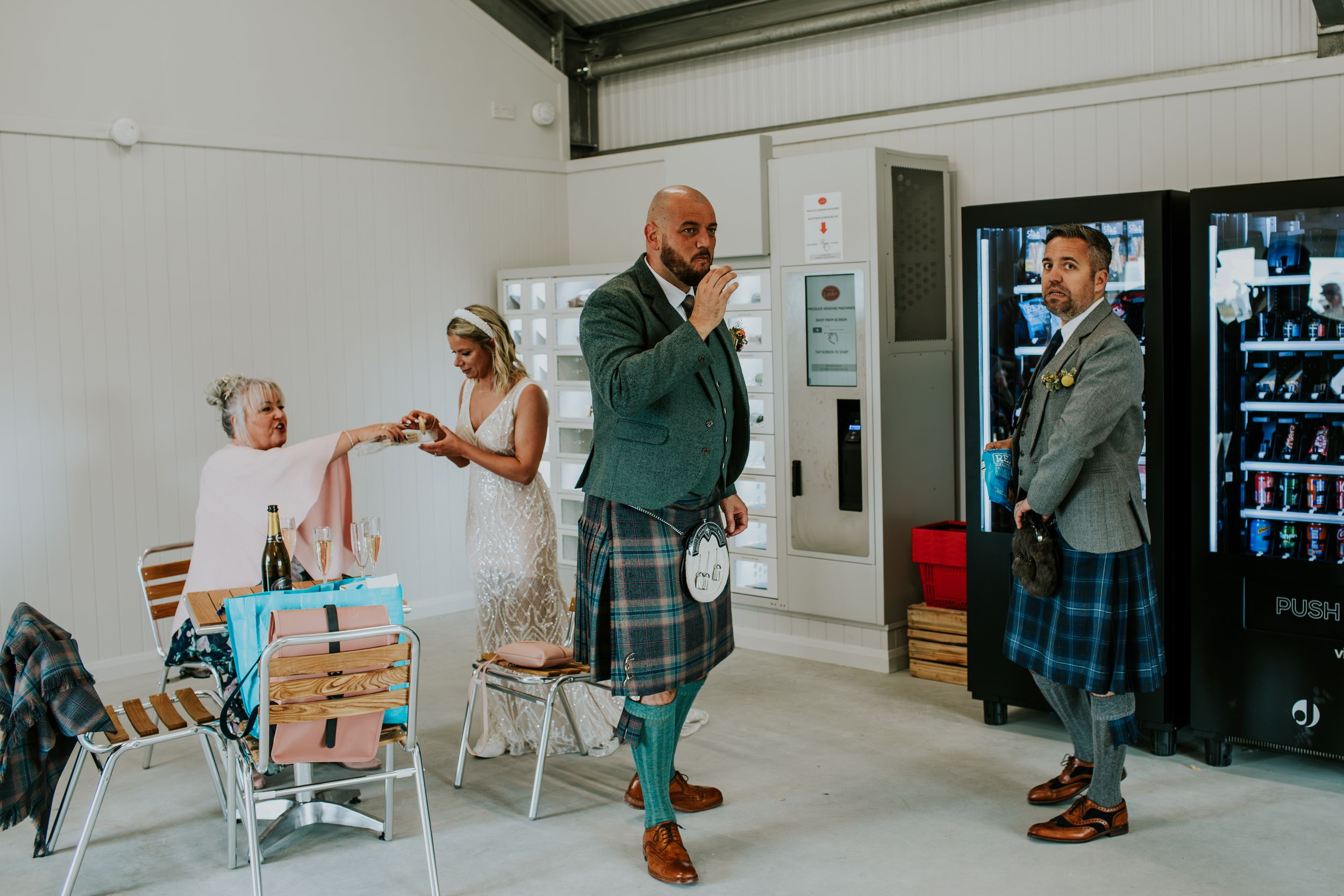Wedding celebration in casual indoor setting with people in Scottish formal wear.