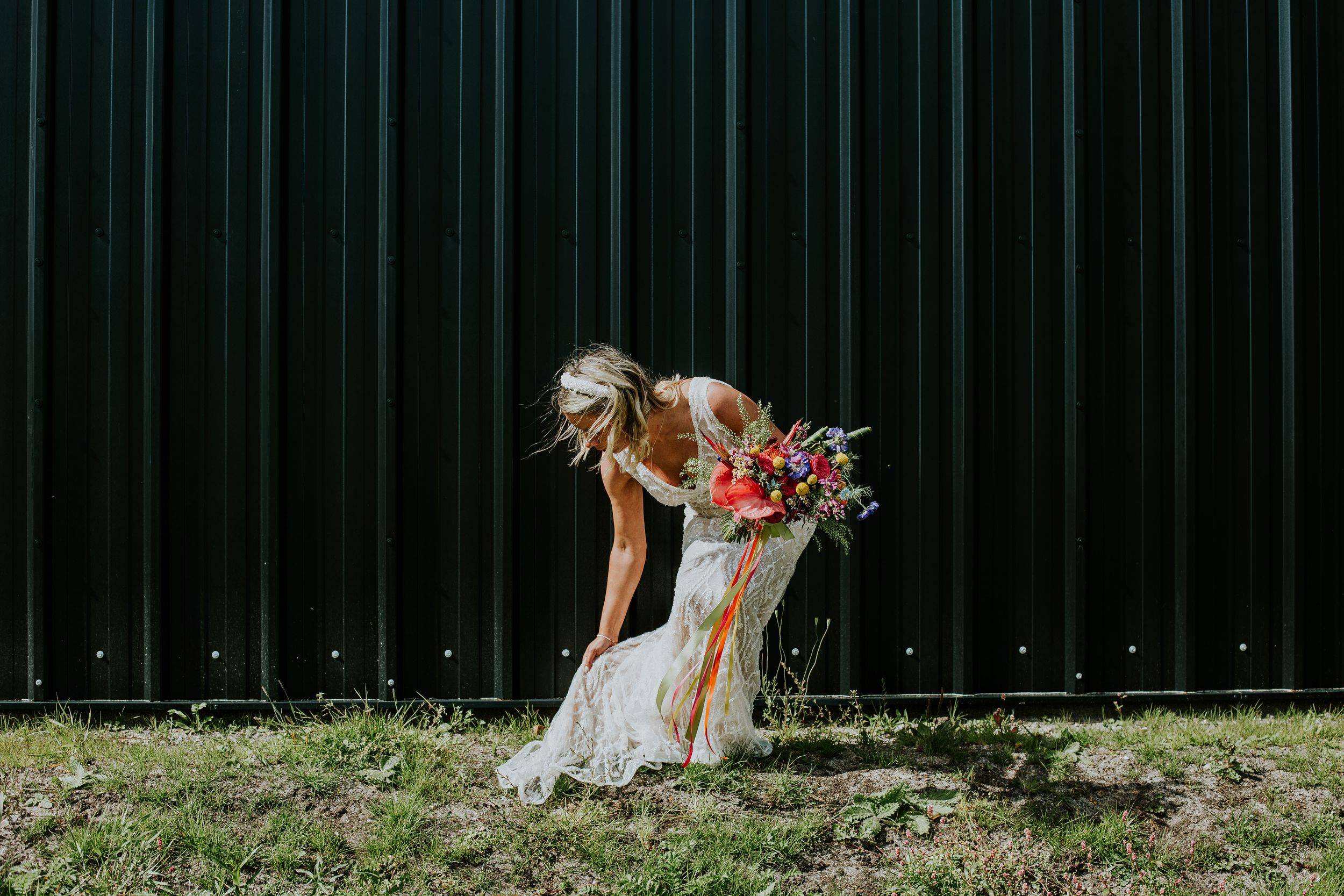 A bride in a white dress bending down to pick up her bouquet against a dark background.